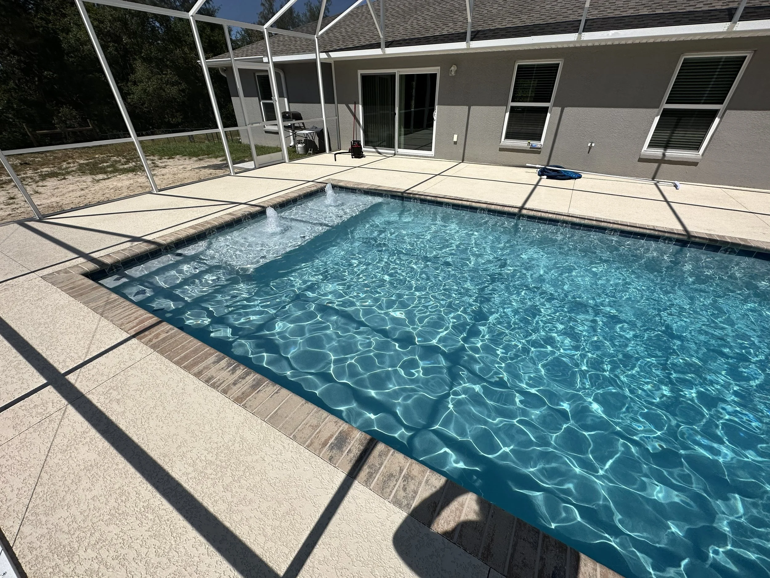Residential backyard with swimming pool, covered with a screened enclosure, and a gray house with multiple windows and a sliding glass door.