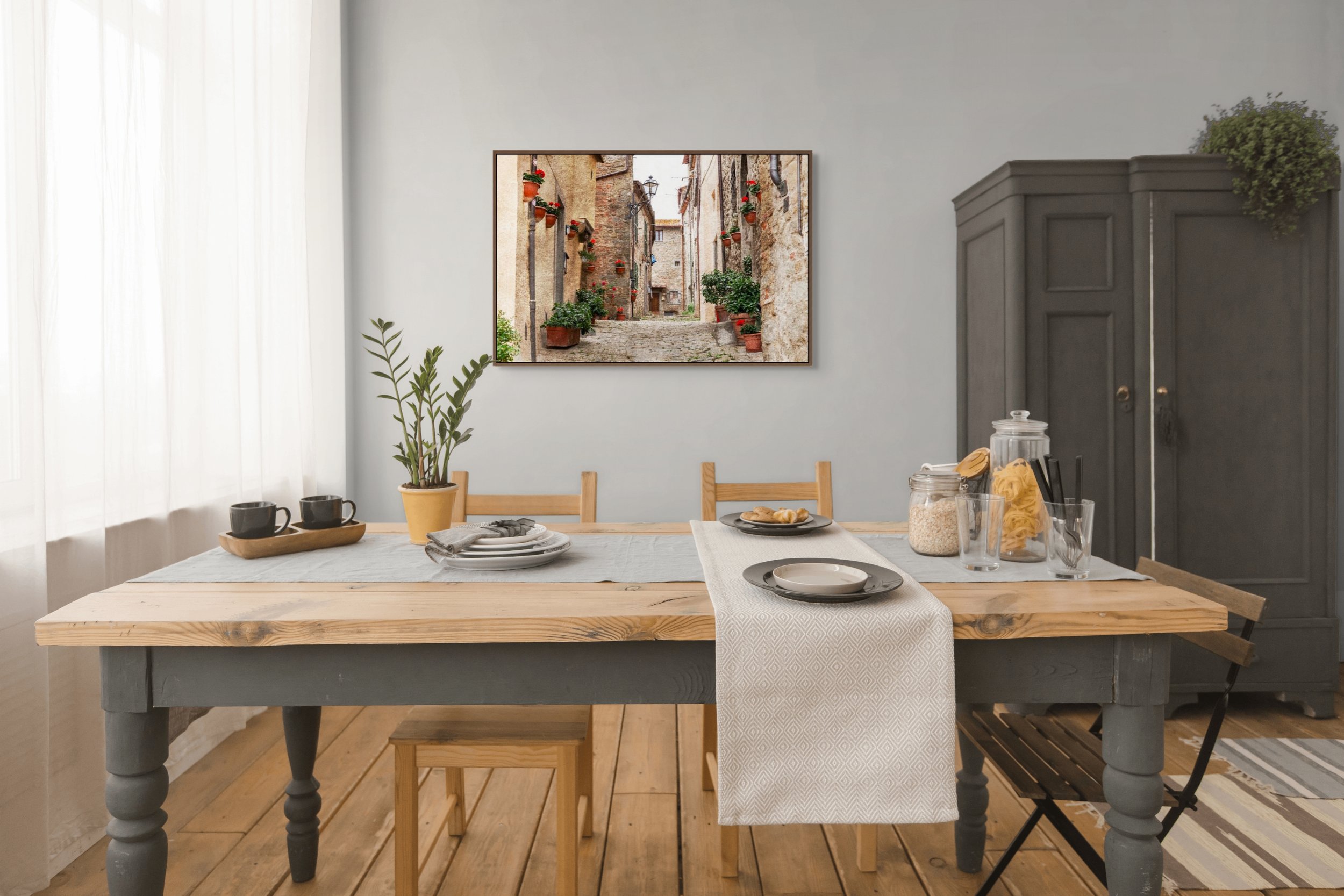 Cobbled street in an Italian village lined with terracotta pots and red geraniums.