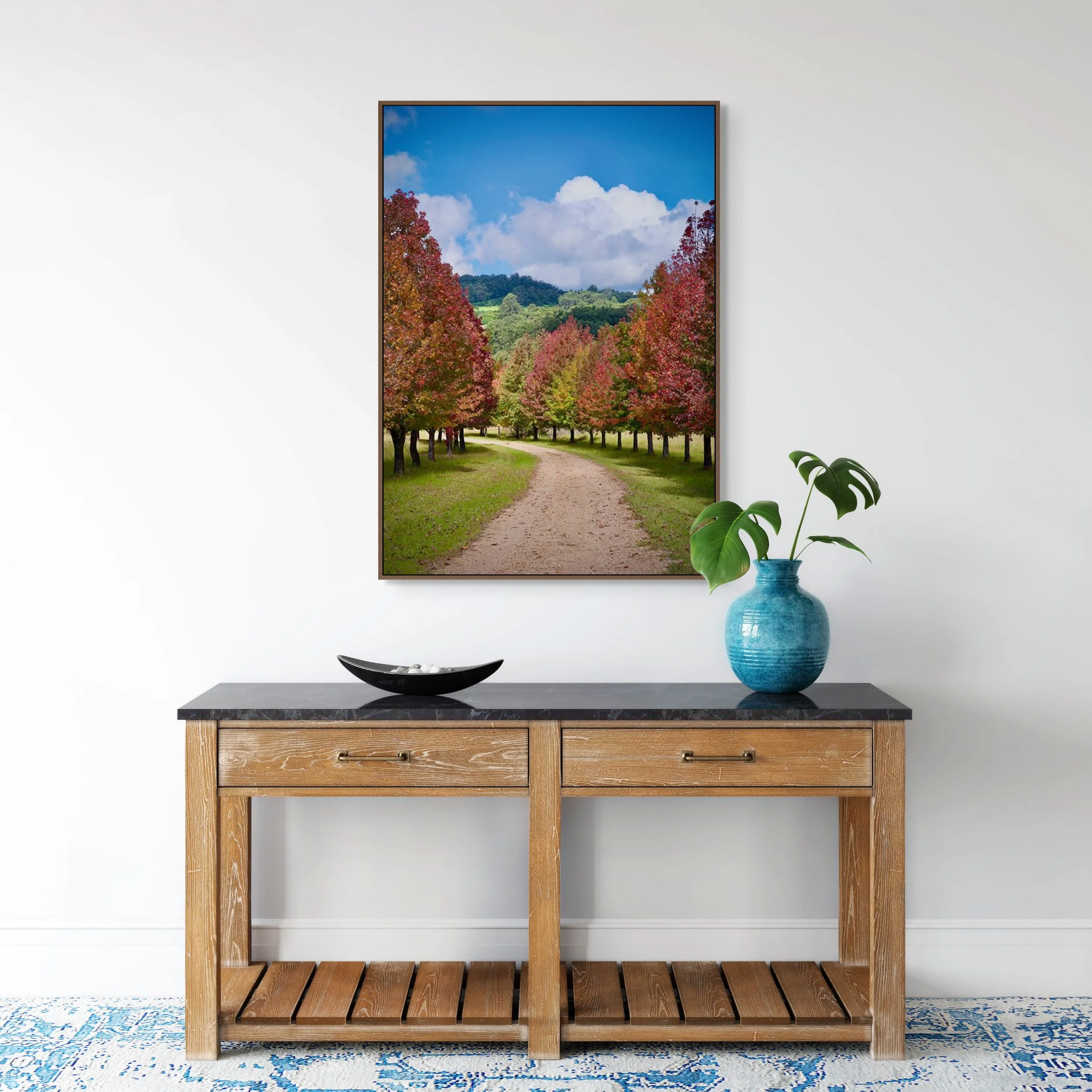 Country path lined with colourful autumn trees leading toward green hills and blue sky.