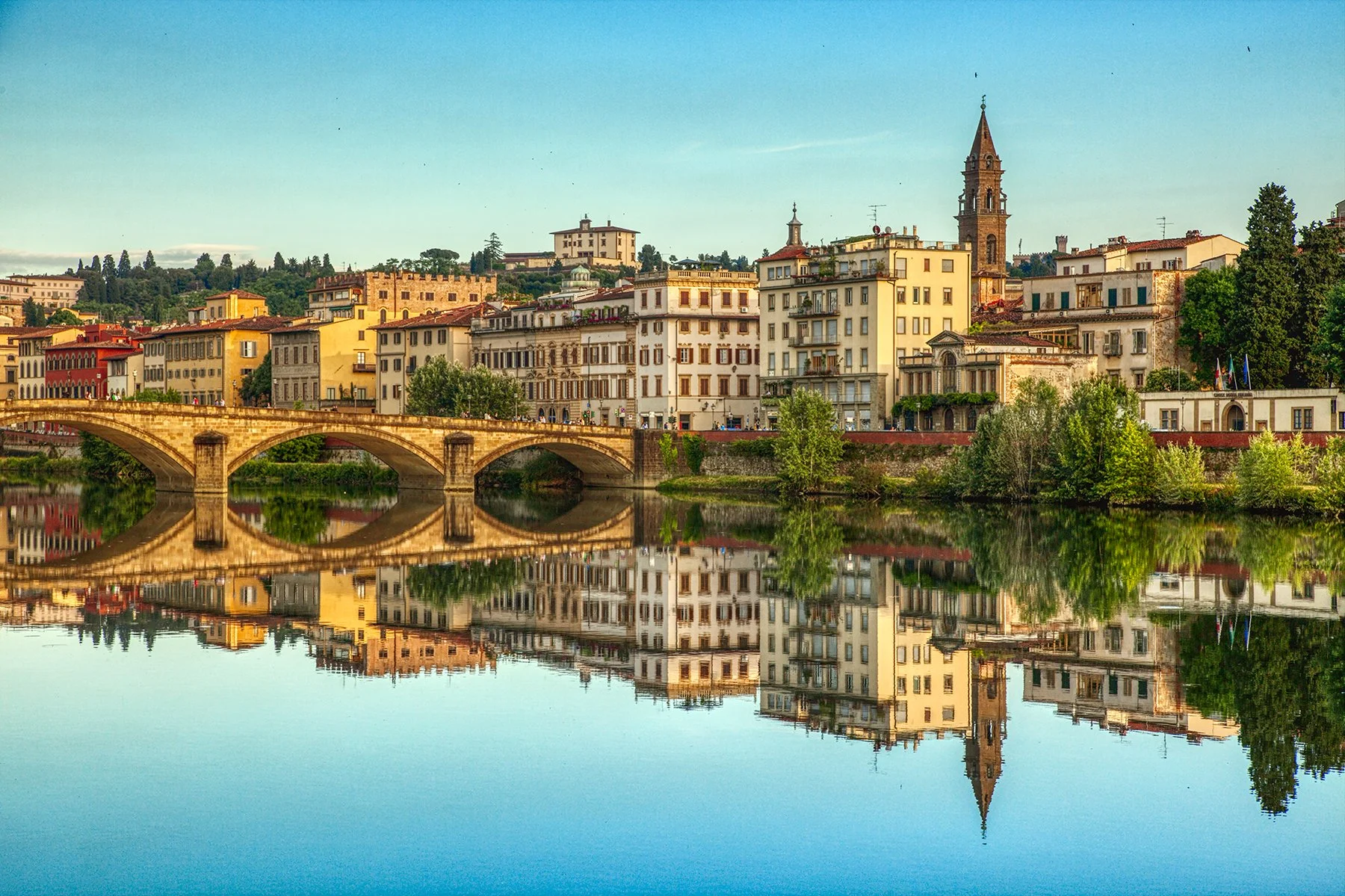 Florence city skyline reflecting in the Arno River with historic bridge and buildings in Italy.