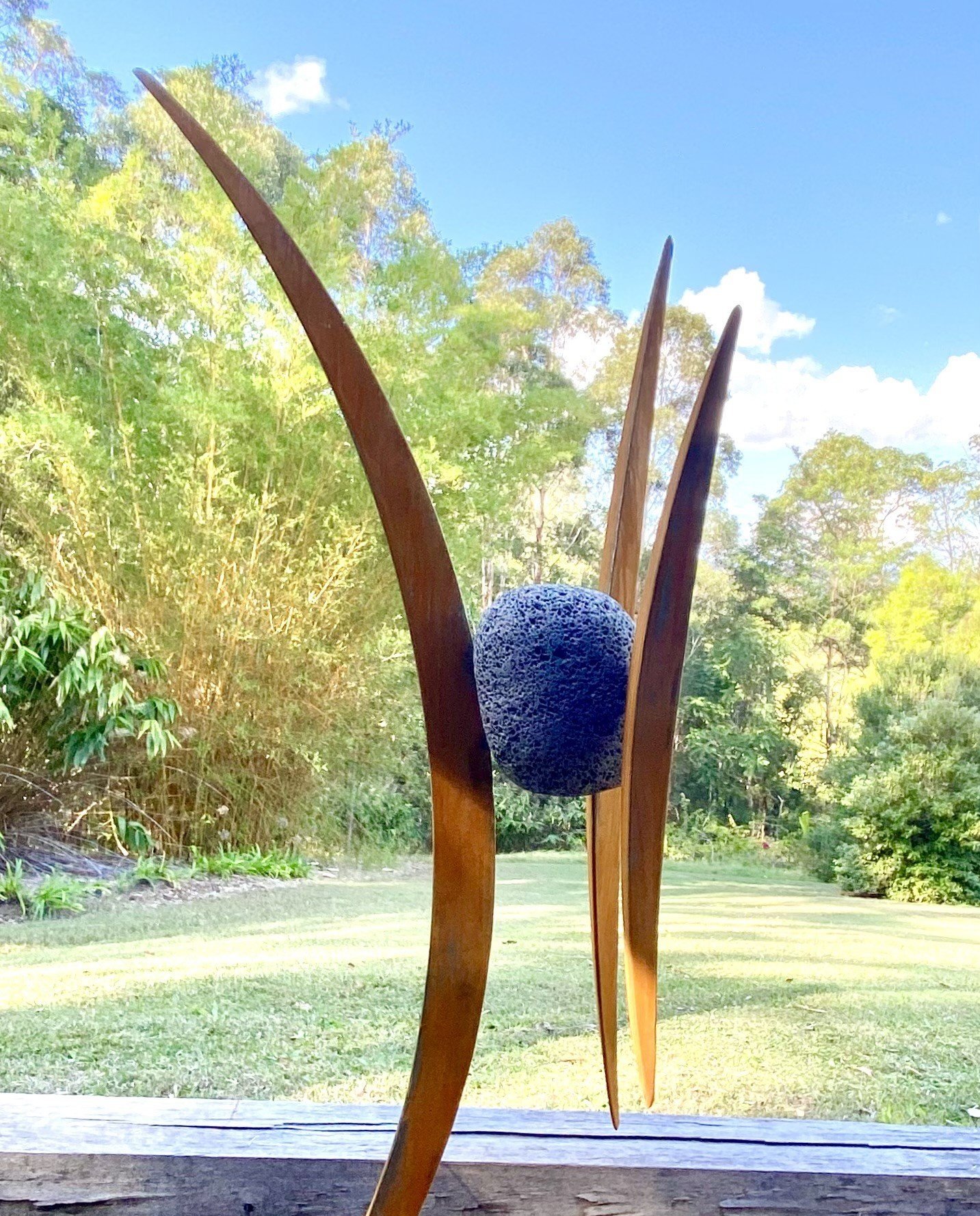 Outdoor sculpture with vertical wooden elements and textured stone against a garden backdrop.