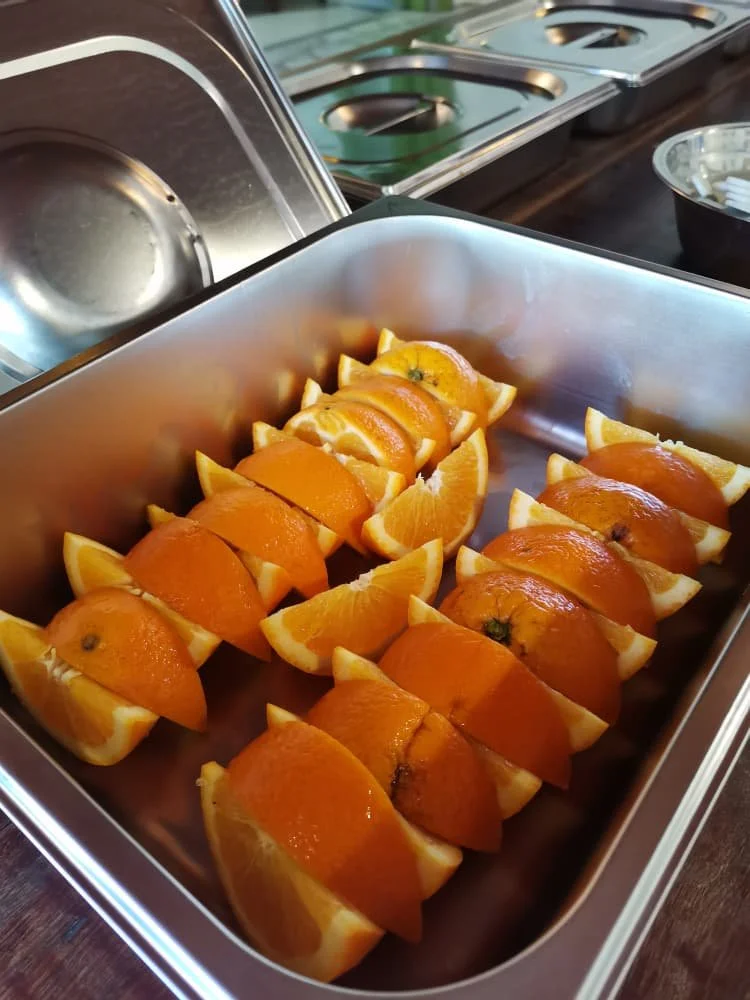 A stainless steel tray filled with orange slices topped with orange halves, arranged in rows on a kitchen countertop.