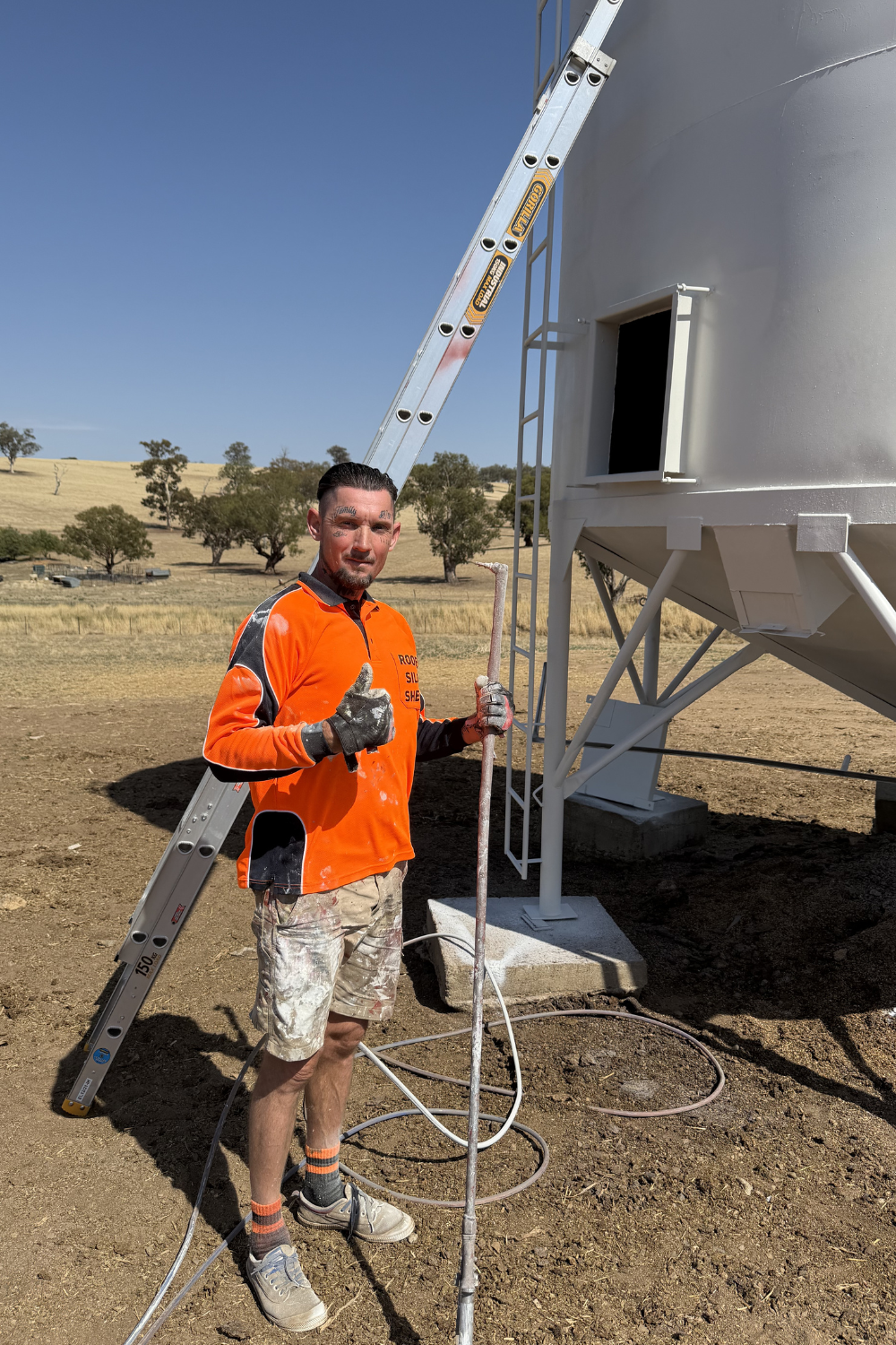 Alfie Hendry of Hendry’s Restorations standing at a freshly painted silo with a paint sprayer.