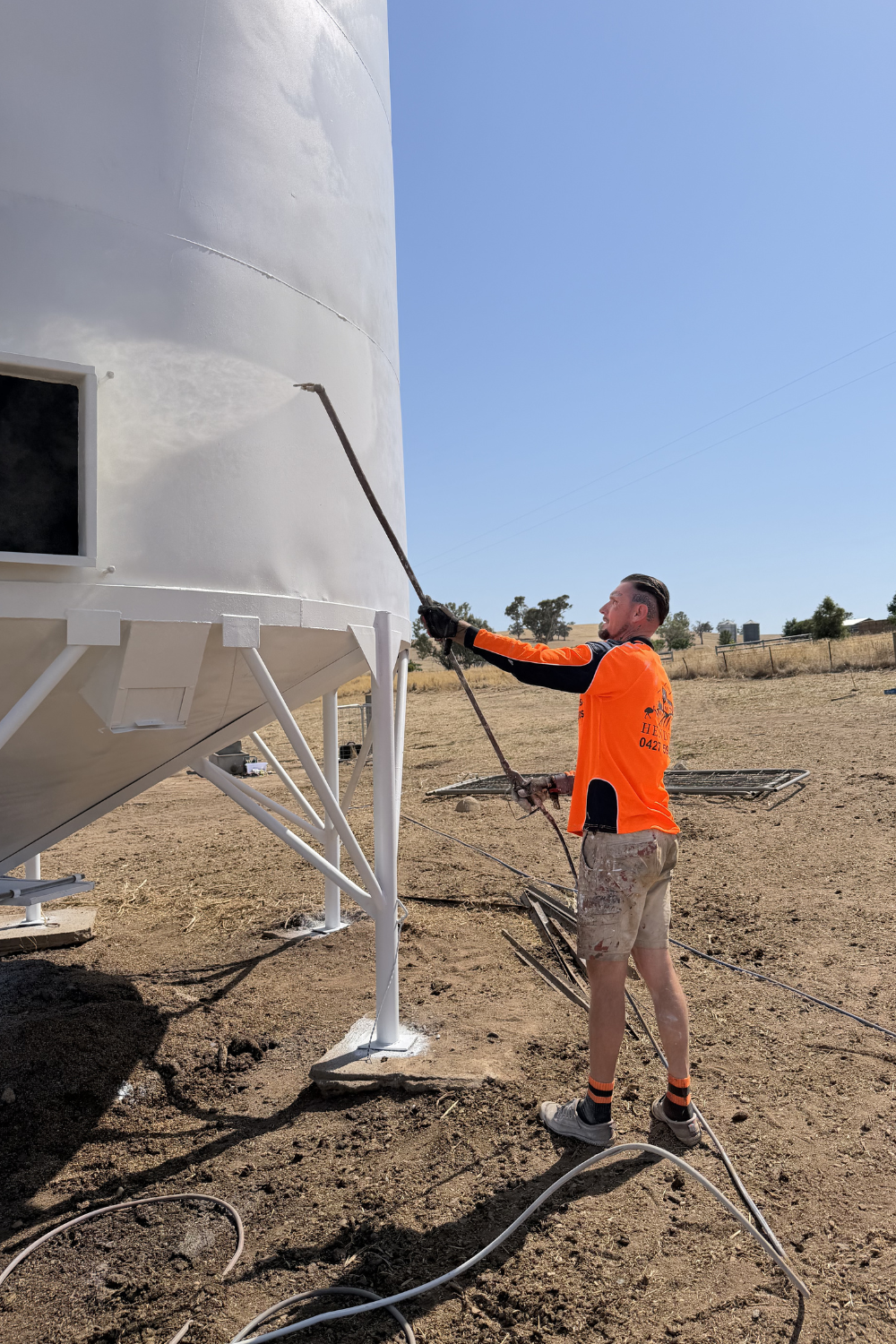 Alfie Hendry, a spray painter, painting a silo in a field in Mungindi.
