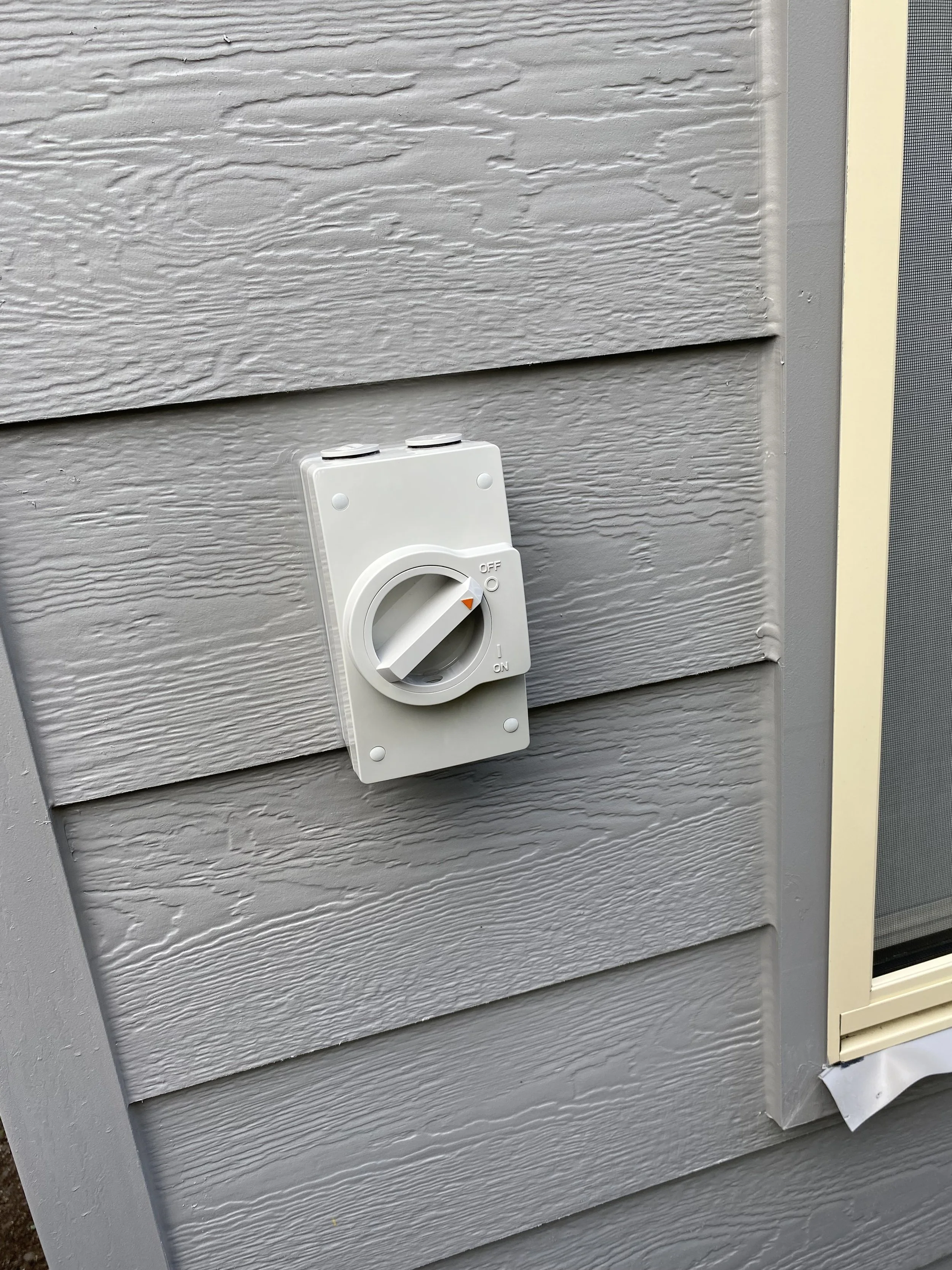 A white rotary switch mounted on the exterior wall of a building, next to a window.
