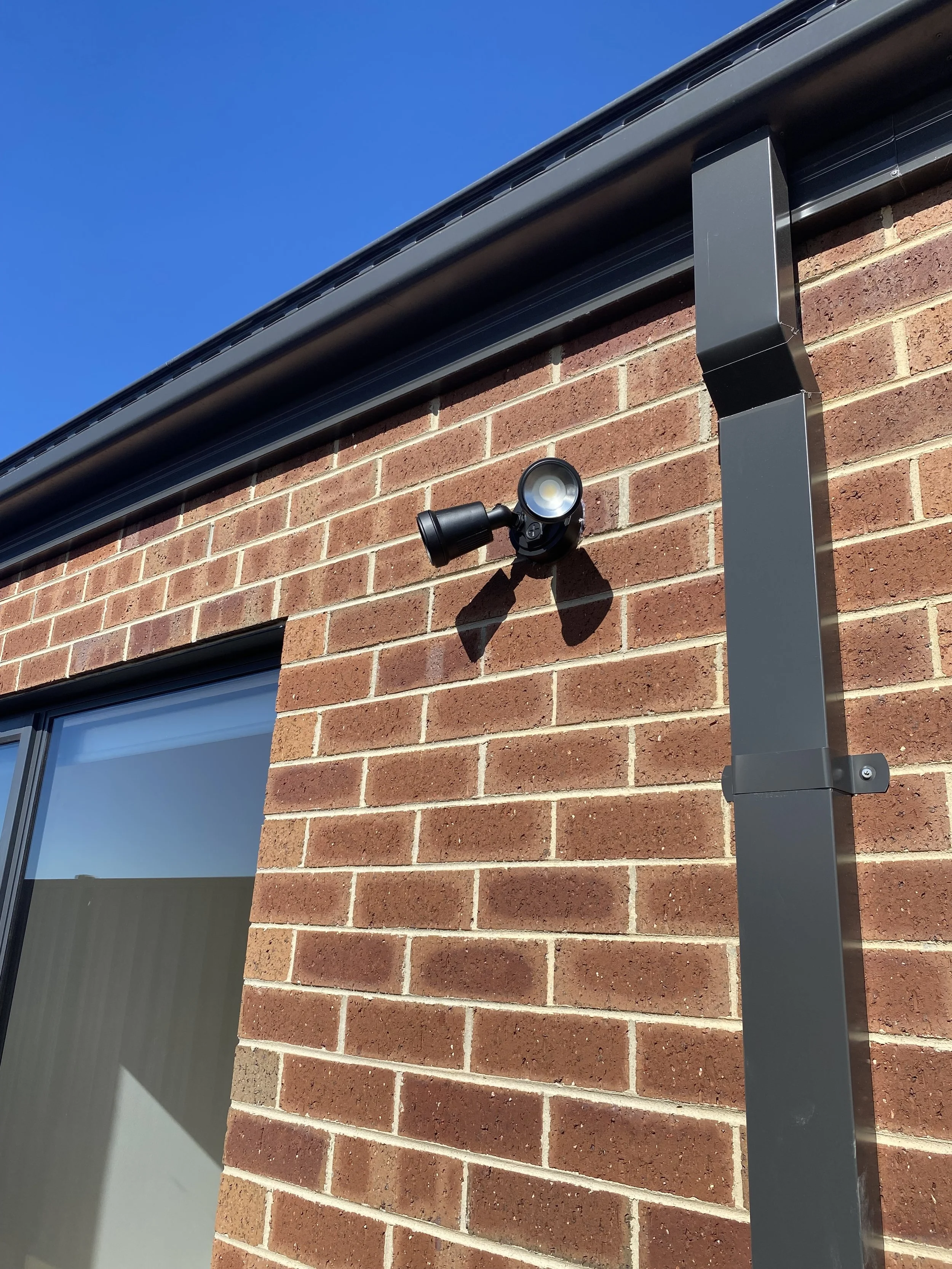 Security camera mounted on the exterior brick wall of a building under a blue sky.