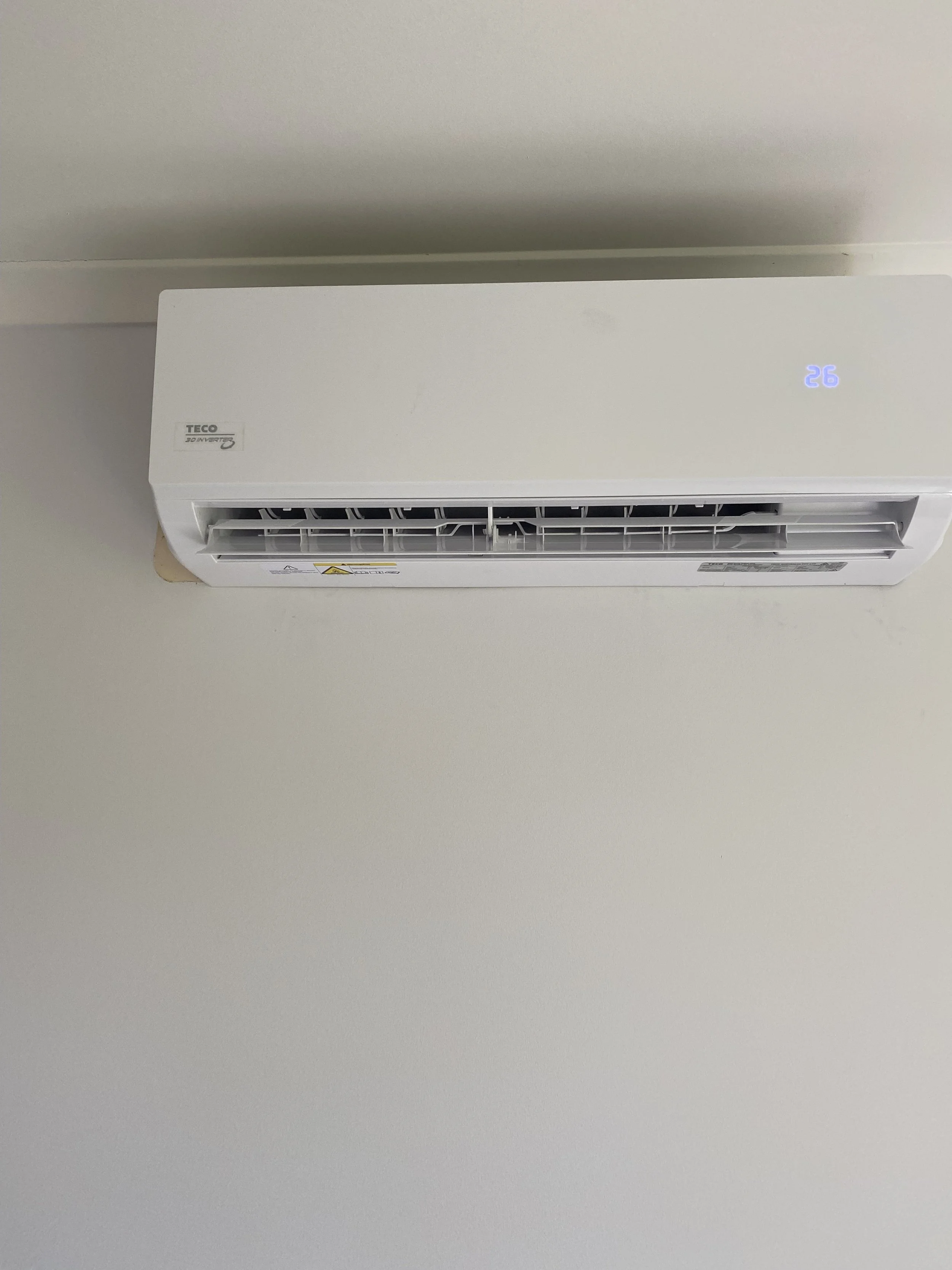 White wall-mounted air conditioning unit displaying temperature of 26 degrees, with vents and black internal components.