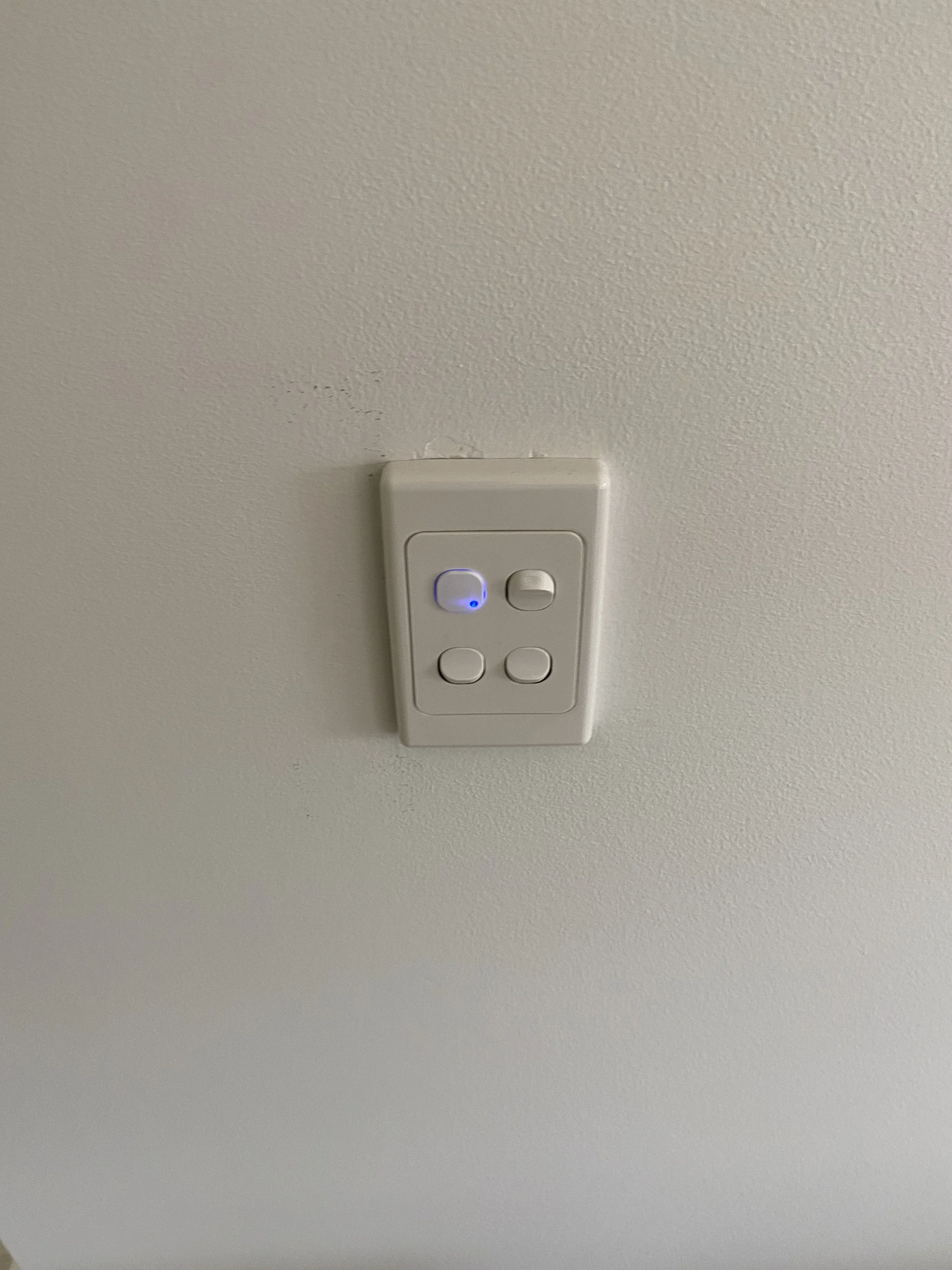 A ceiling-mounted remote control with four buttons, one of which is illuminated with a blue indicator light.