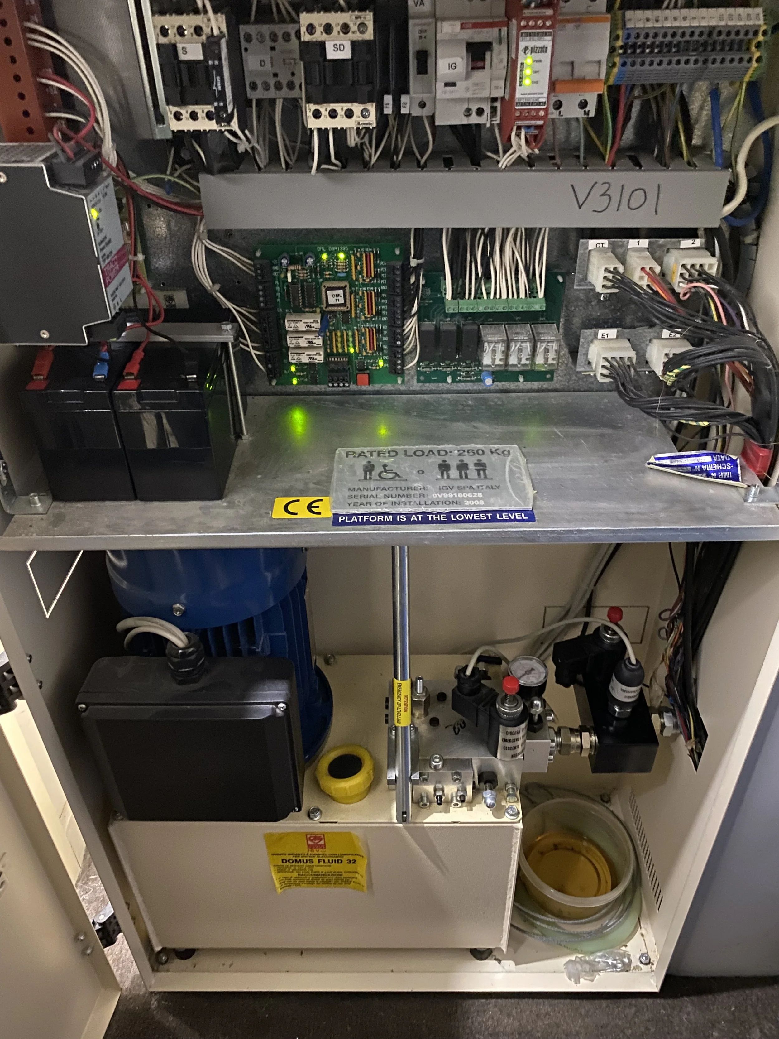 Electrical control panel with various wires, switches, a circuit board, and a hydraulic fluid reservoir.