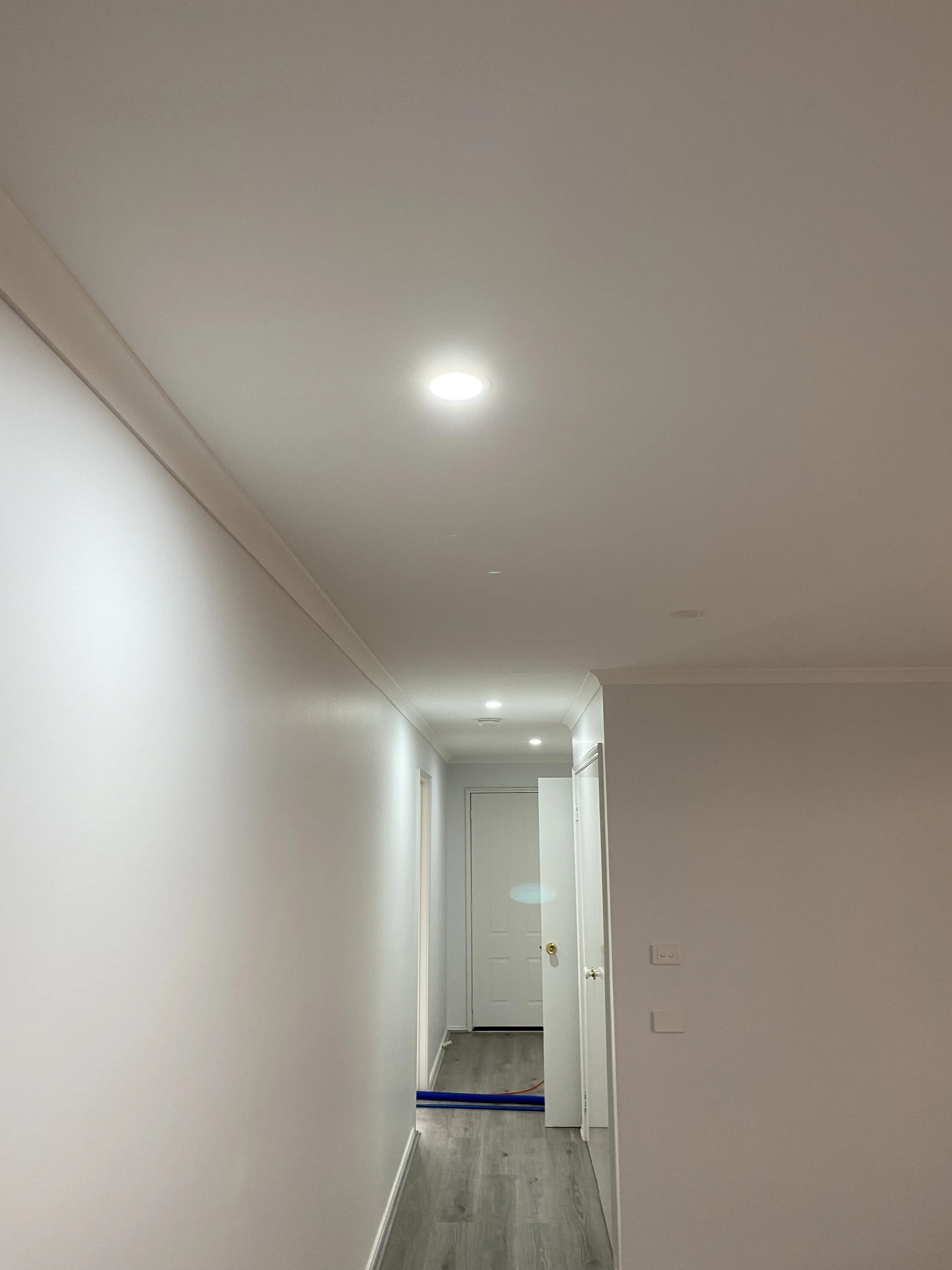 Empty hallway with white walls, wooden flooring, and ceiling lights in a modern home.