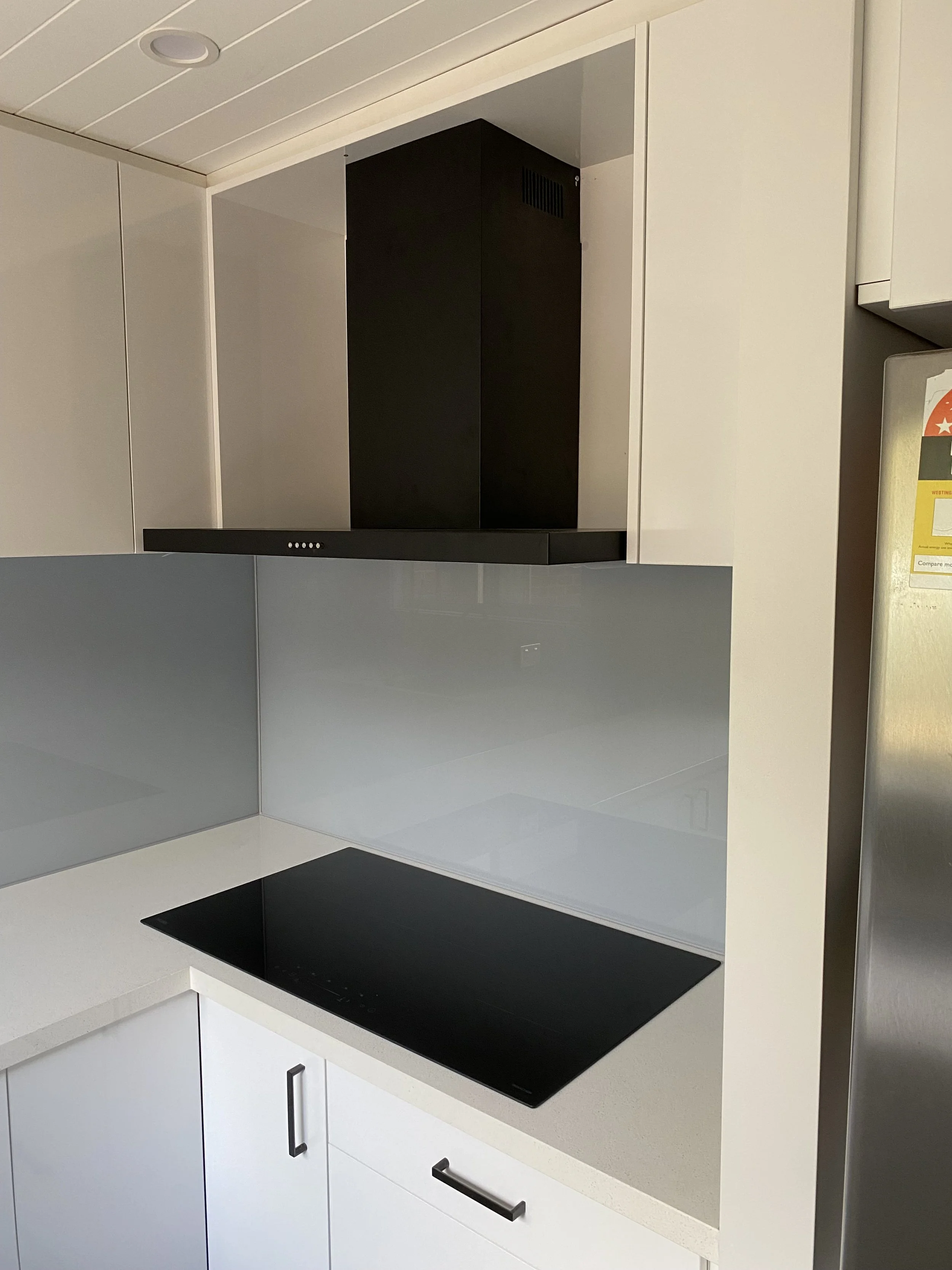 Modern kitchen with a white countertop, black electric cooktop, light-colored cabinets, and a black range hood.