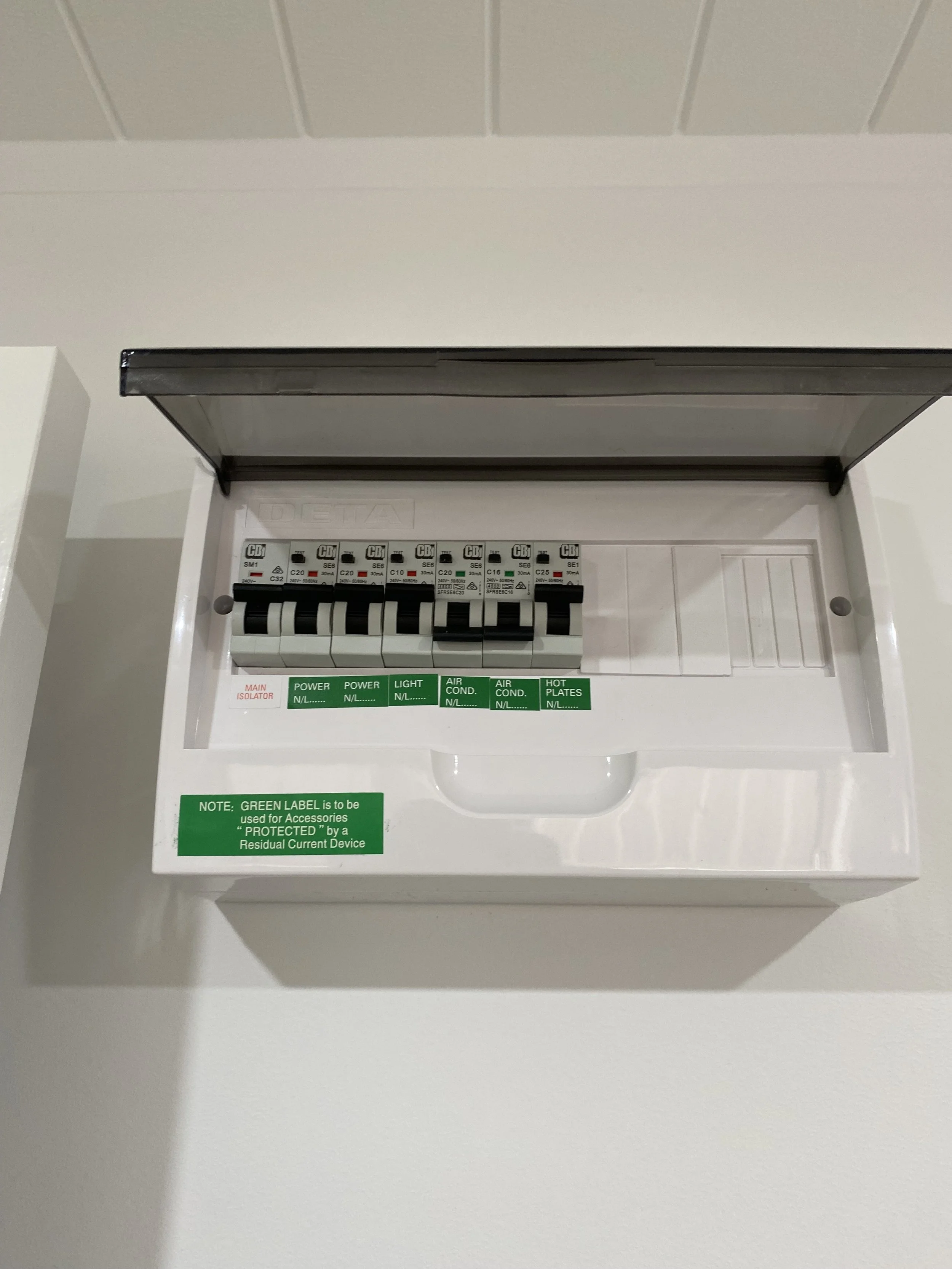 Electrical circuit breaker panel with multiple switches and green labels indicating power, light, air conditioning, and hot plates.