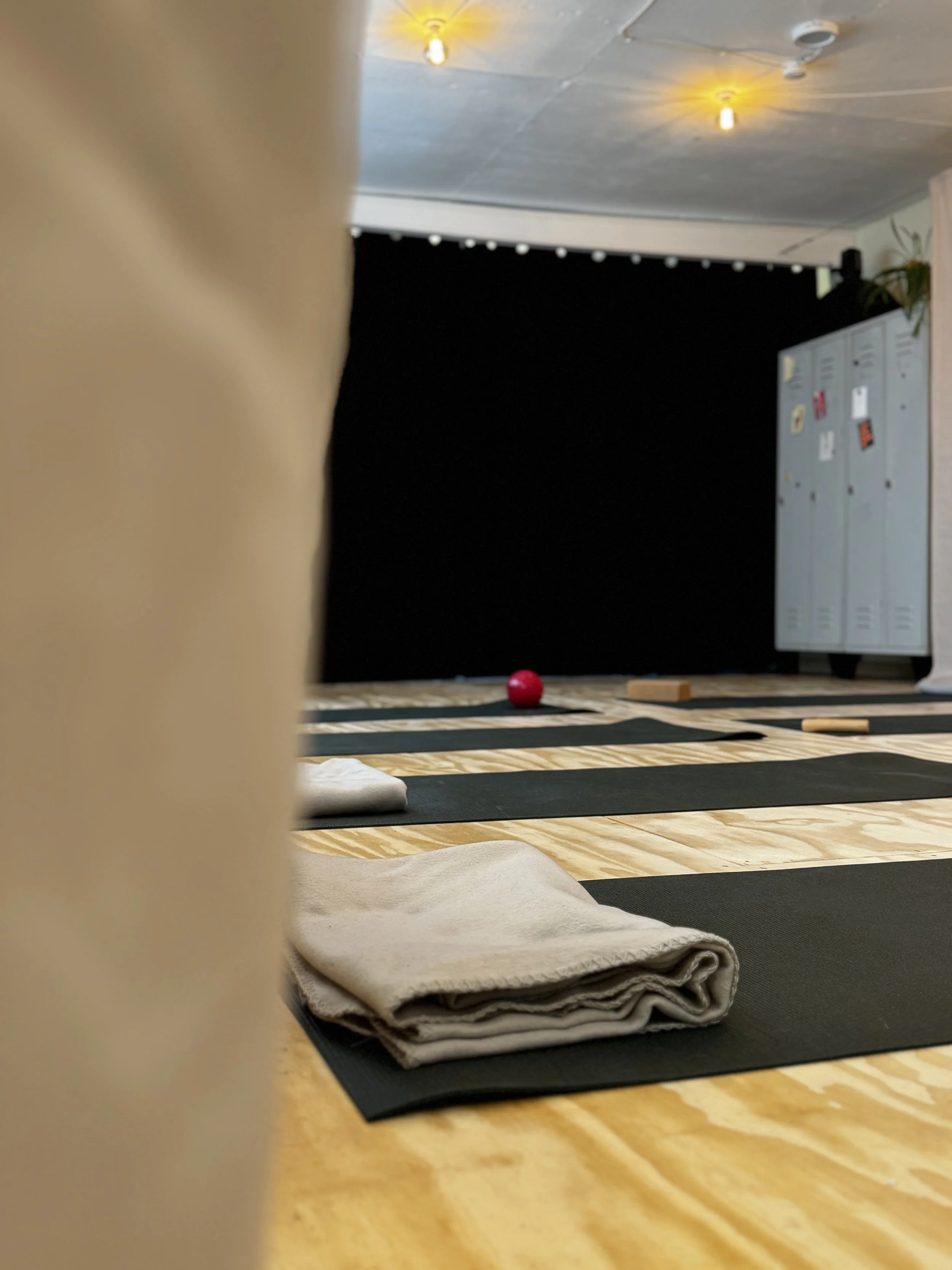 Yogamatten, Handtücher und eine rote Kugel in einem Raum mit dunklem Hintergrund, vermutlich für Yoga oder Meditation.
