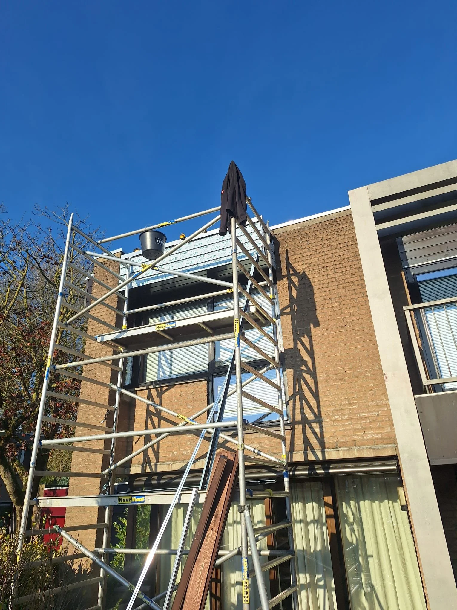 Scaffolding set up outside a multi-story building with brick and modern concrete exterior, under a clear blue sky.