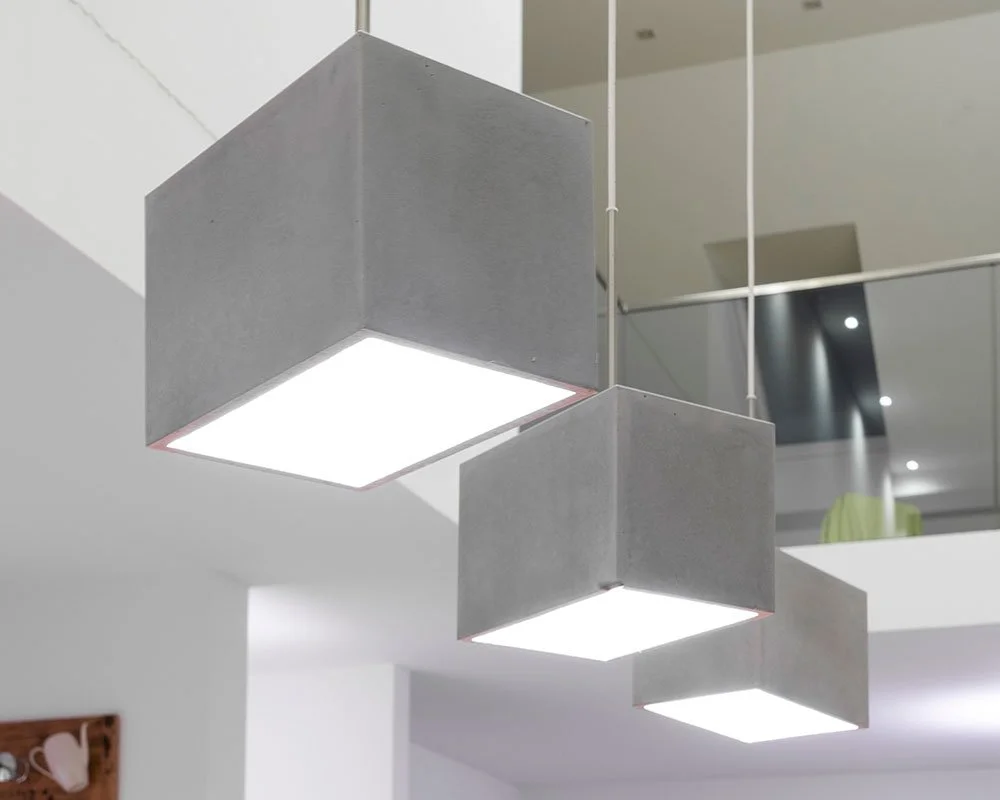 Drei moderne graue quadratische Hängelampen mit LED-Beleuchtung hängen von der Decke in einem Raum.