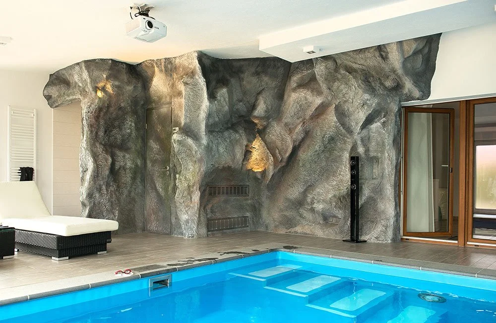Innenansicht eines Hauses mit einem kleinen Pool, einer künstlichen Felswand und einer gläsernen Balkon- oder Terrassentür.