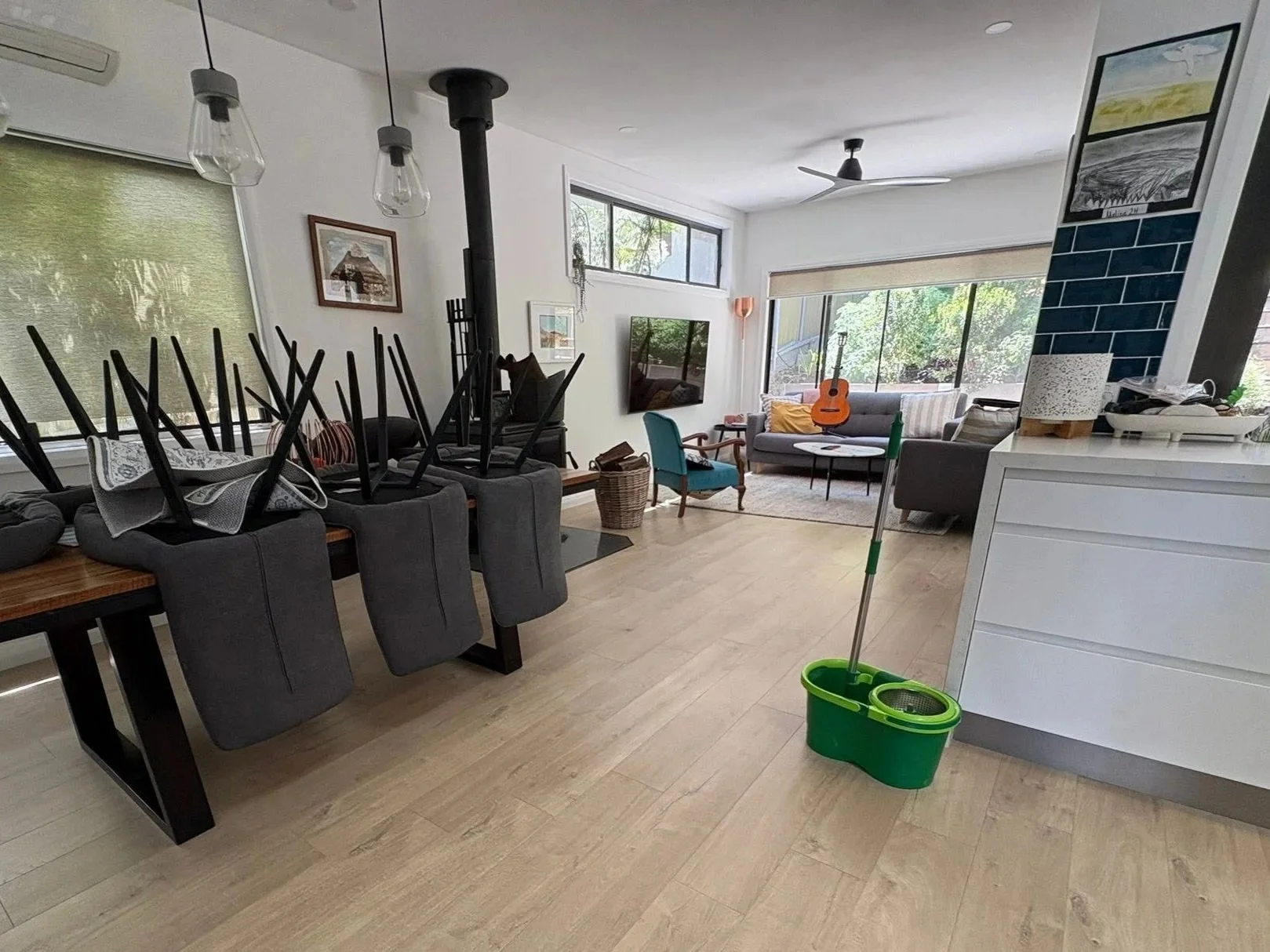 Living room with furniture and a large window, a guitar, and a mop in a green bucket.