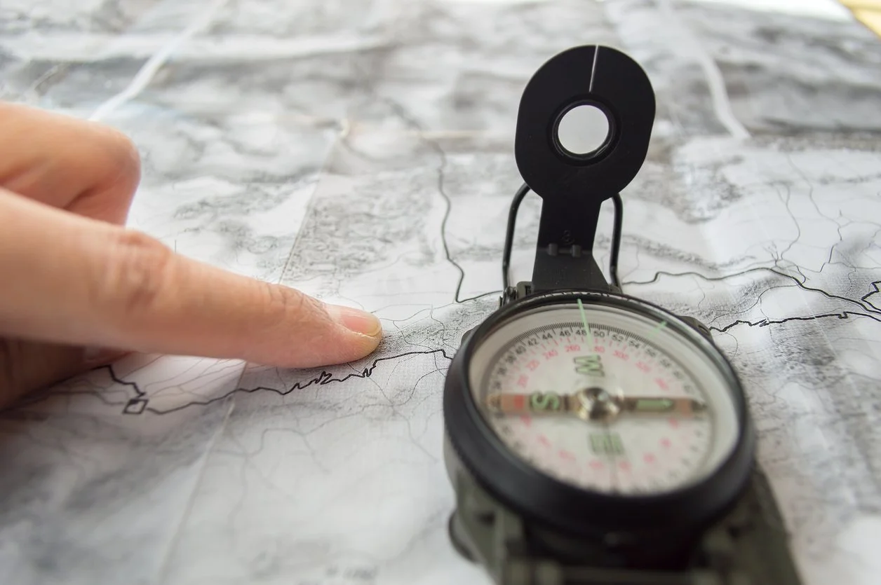 Close-up of a hand pointing at a map with a compass on top.