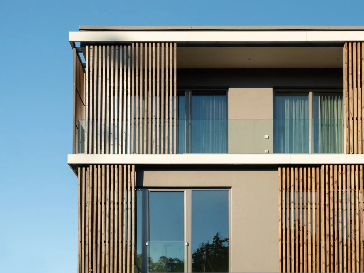 Modern building facade with wooden slats, large windows, and blue sky background.