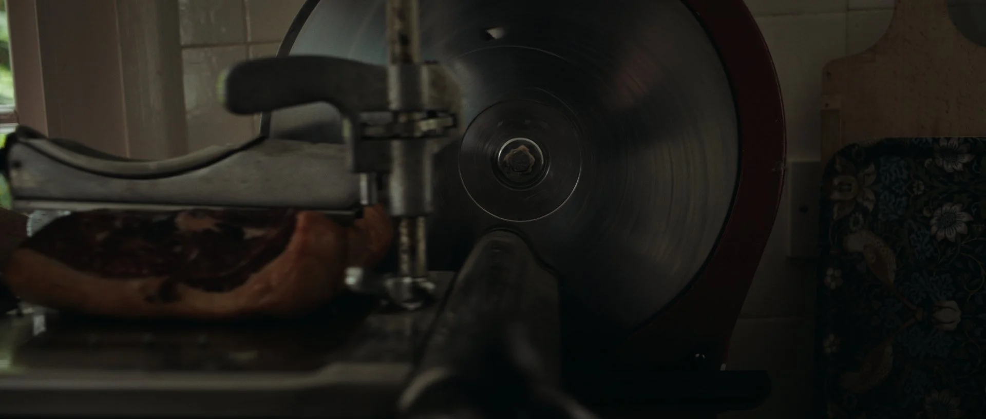 Close-up of a vintage meat slicer cutting home-cured bacon, rich reds and deep shadows adding cinematic depth