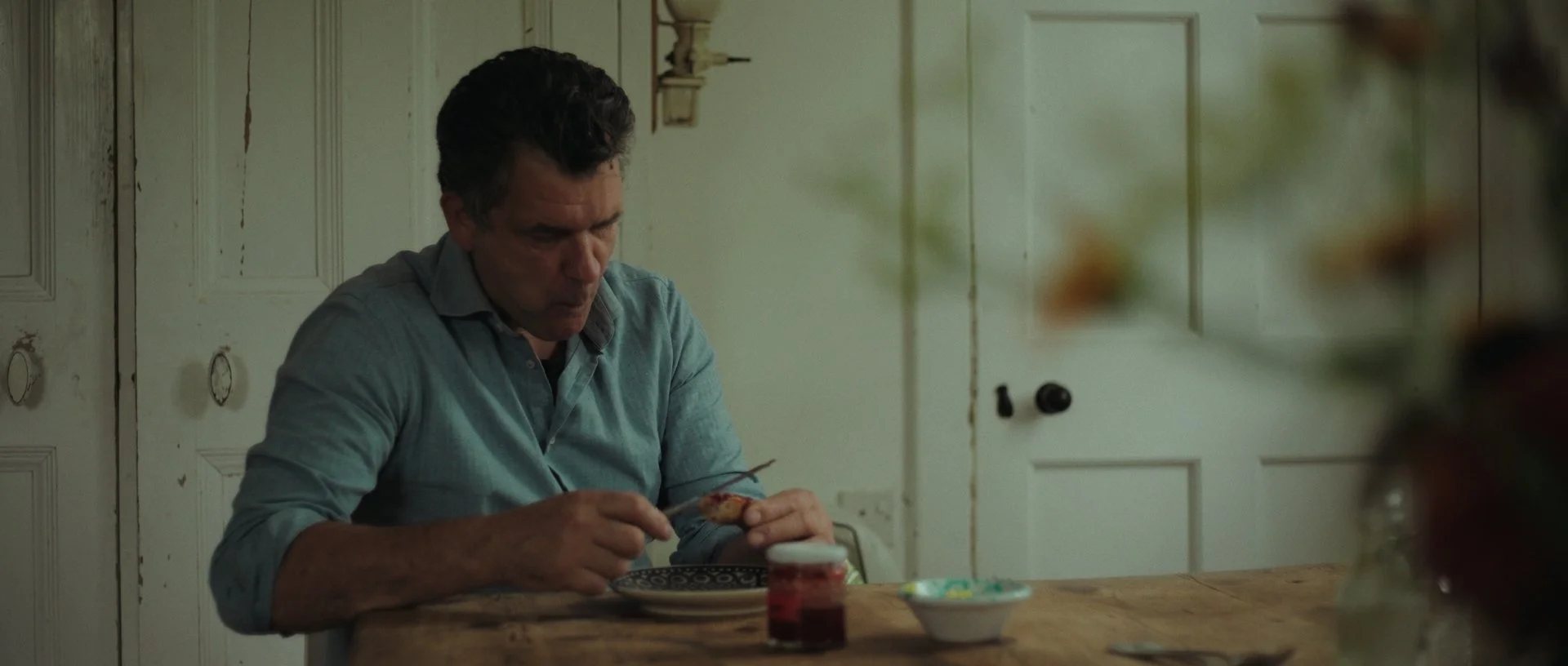 In a stunning farmhouse kitchen, enjoying a scone with jam, filmic tones adding warmth and nostalgia