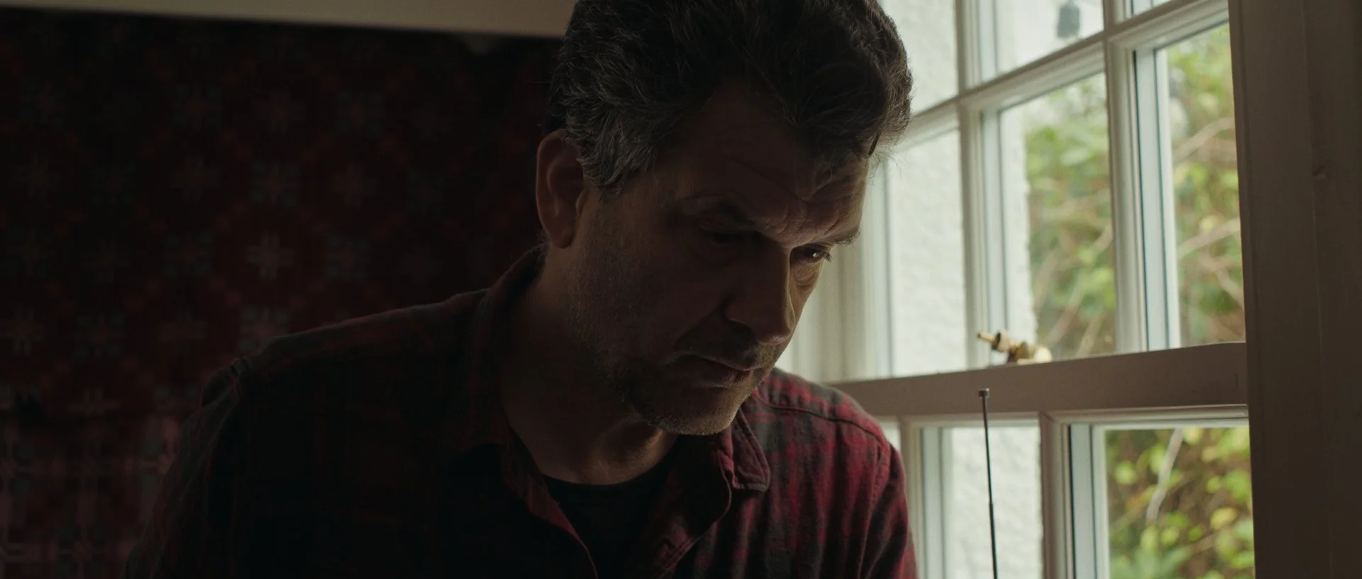 Side profile of Jan Jacob slicing bacon, natural light sculpting his silhouette in a painterly, filmic style