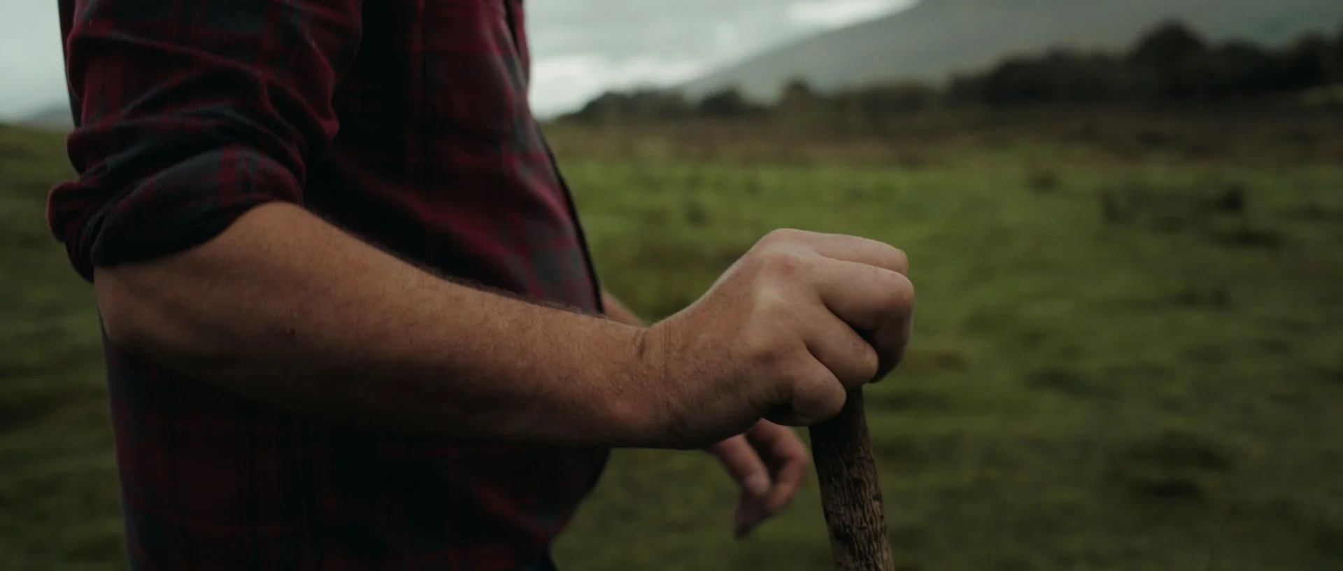Jan Jacob’s weathered hand gripping a walking stick, textures emphasised in a rich, earthy palette