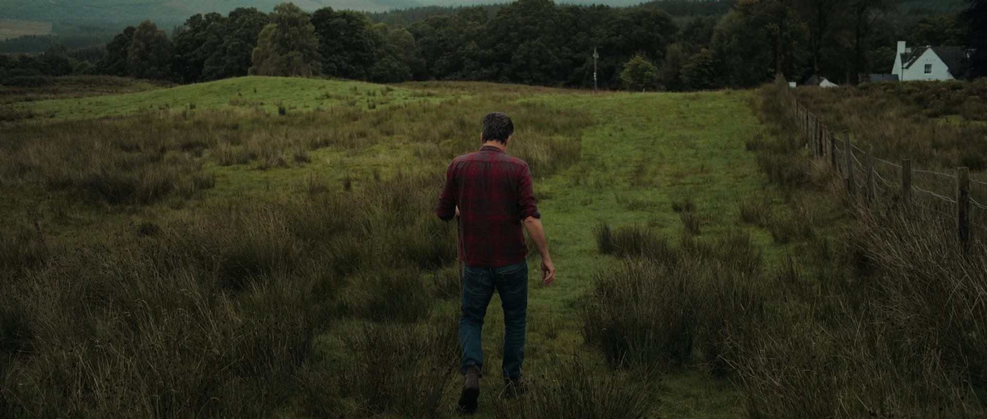 Jan Jacob walking away from the closed gate, the vast landscape unfolding behind him in rich tones
