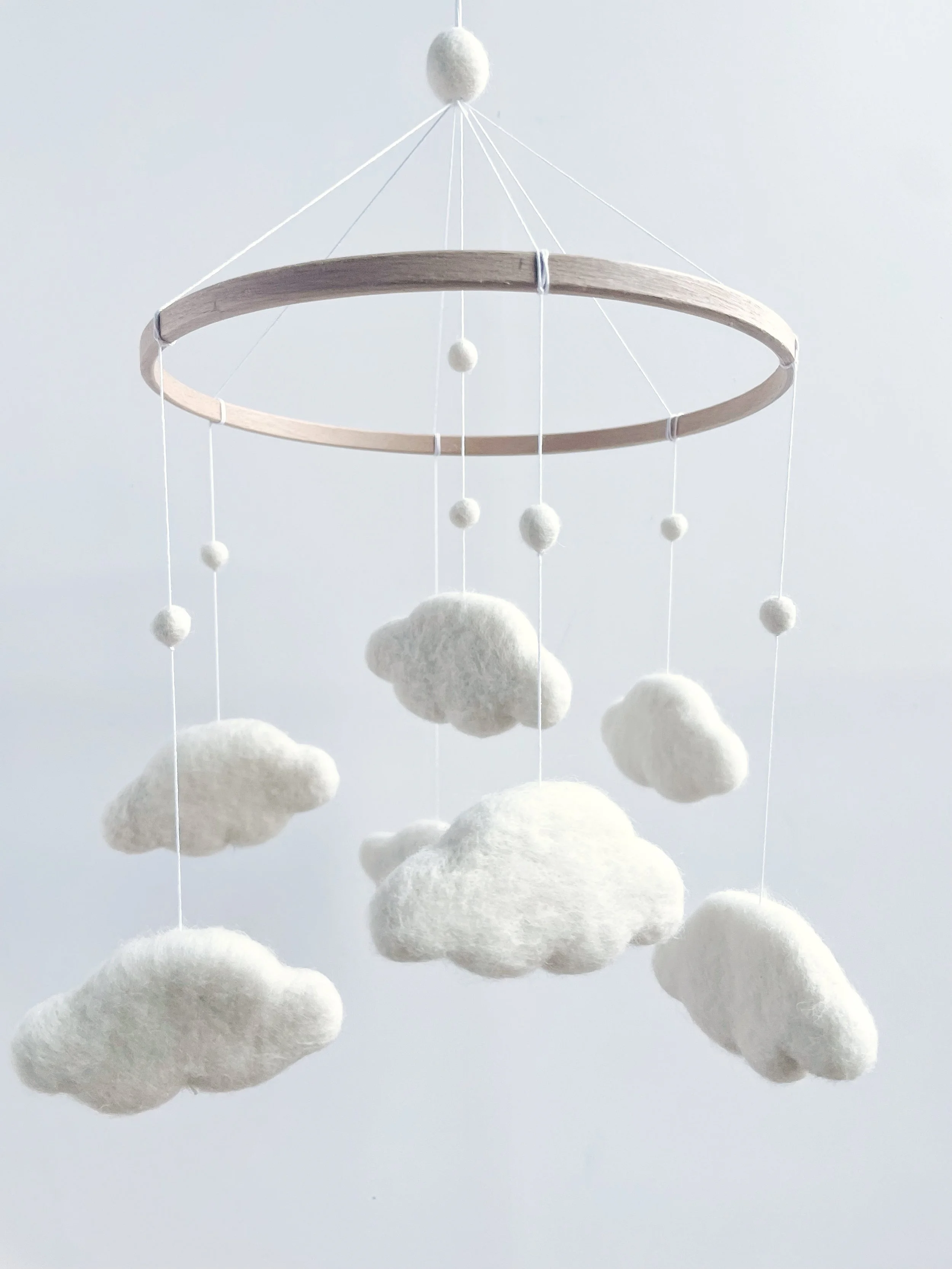 White felt clouds and felt balls threaded onto string and attached to a wooden hoop.