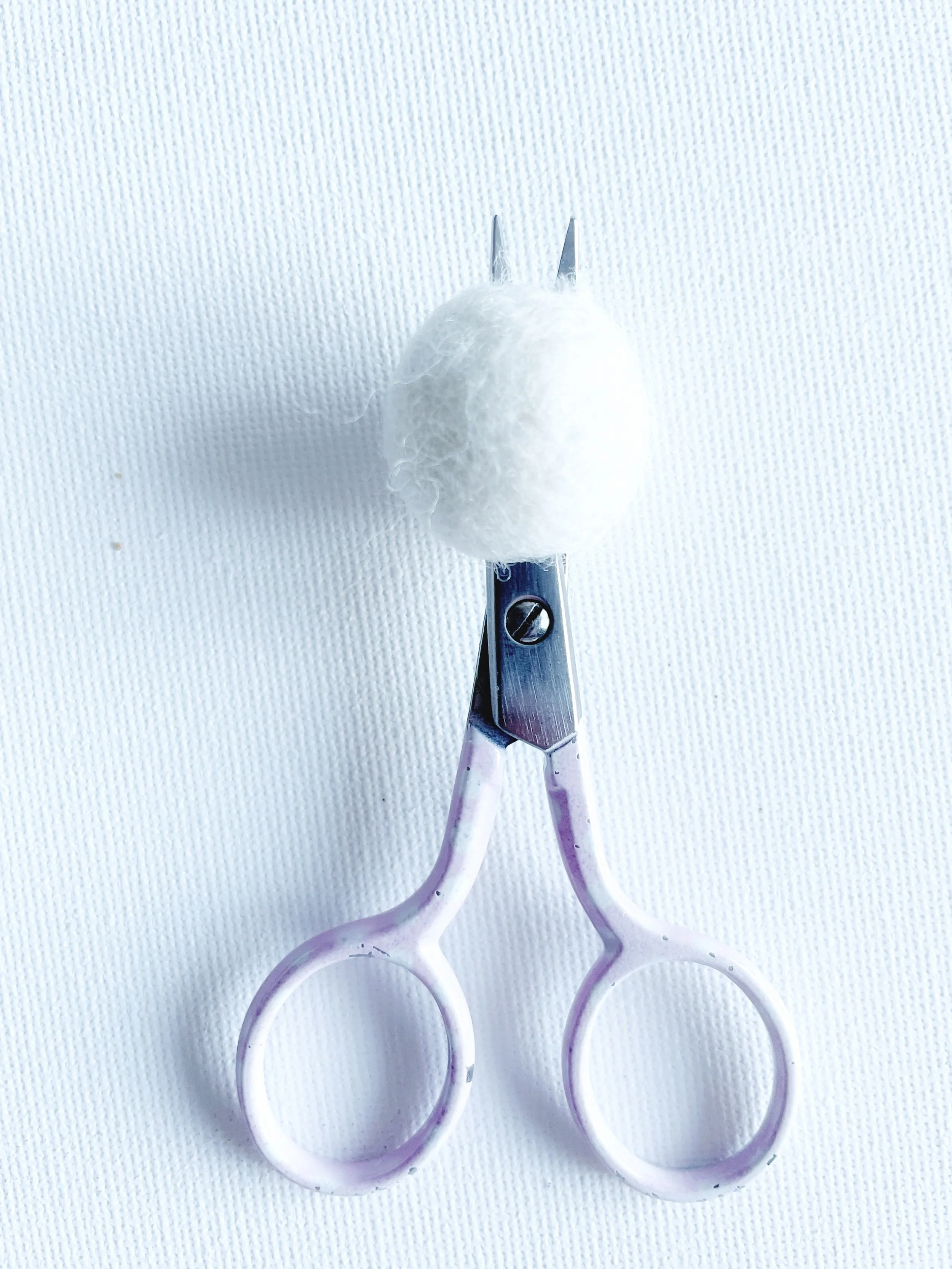Small, pink handled scissors cutting in to white felt ball
