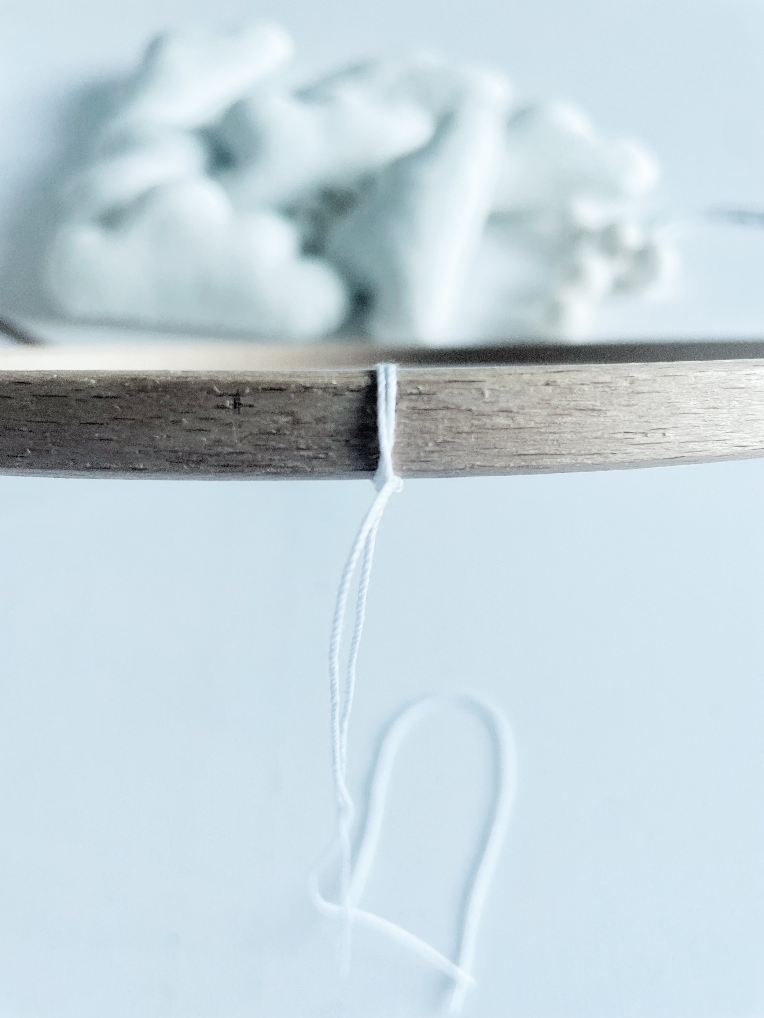 Wooden hoop with white string tied to it with knot. String dangles down from knot.