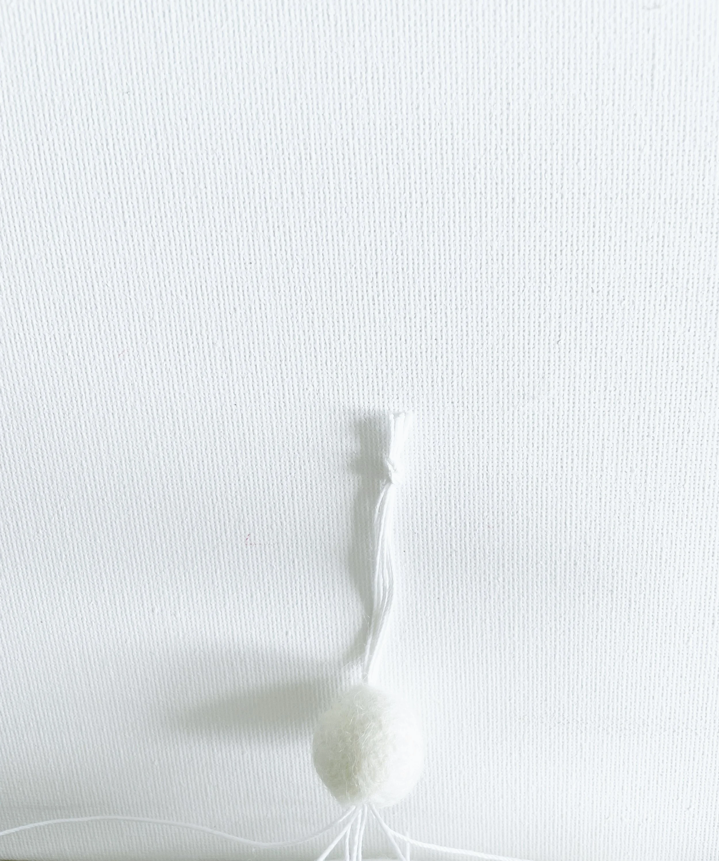 White felt ball threaded onto string with a knotted loop above it