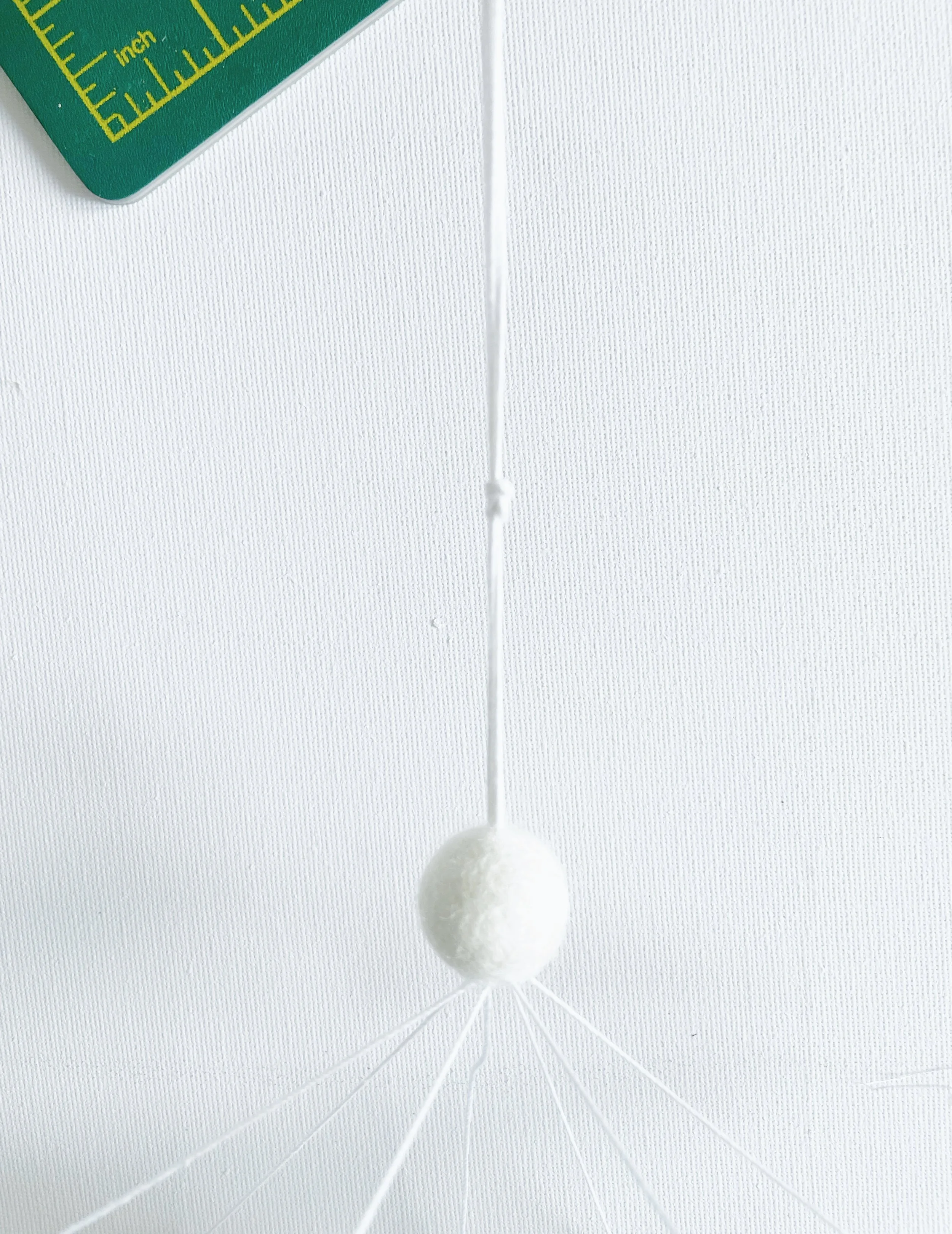 White felt ball threaded onto white string with a knot tied an inch above felt ball.