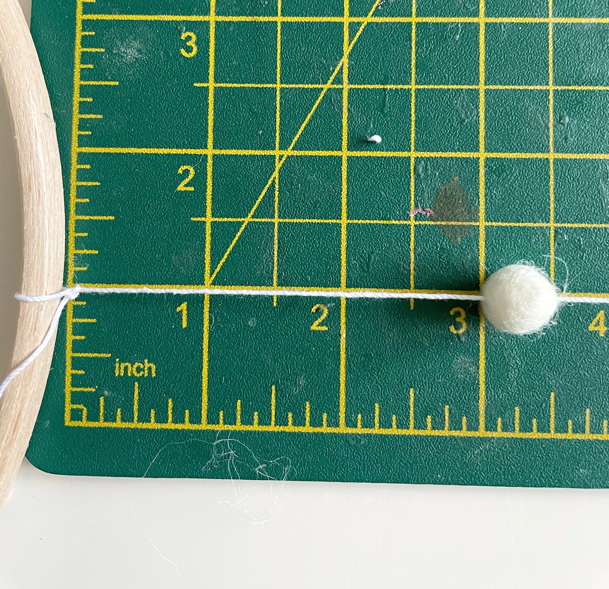White string threaded with a white felt ball. Measured on a green cutting mat.