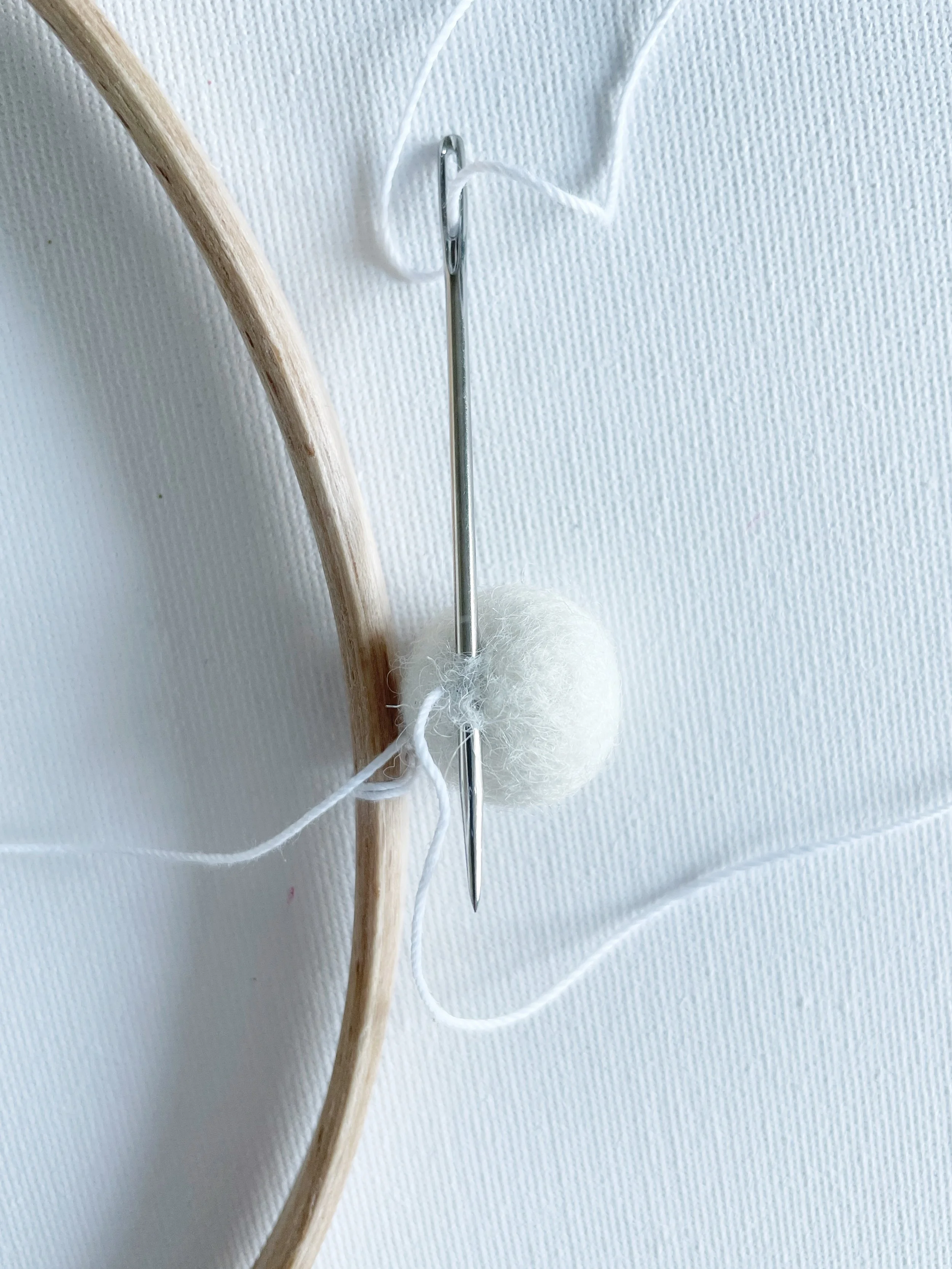 White felt ball with sewing needle and string threaded through base