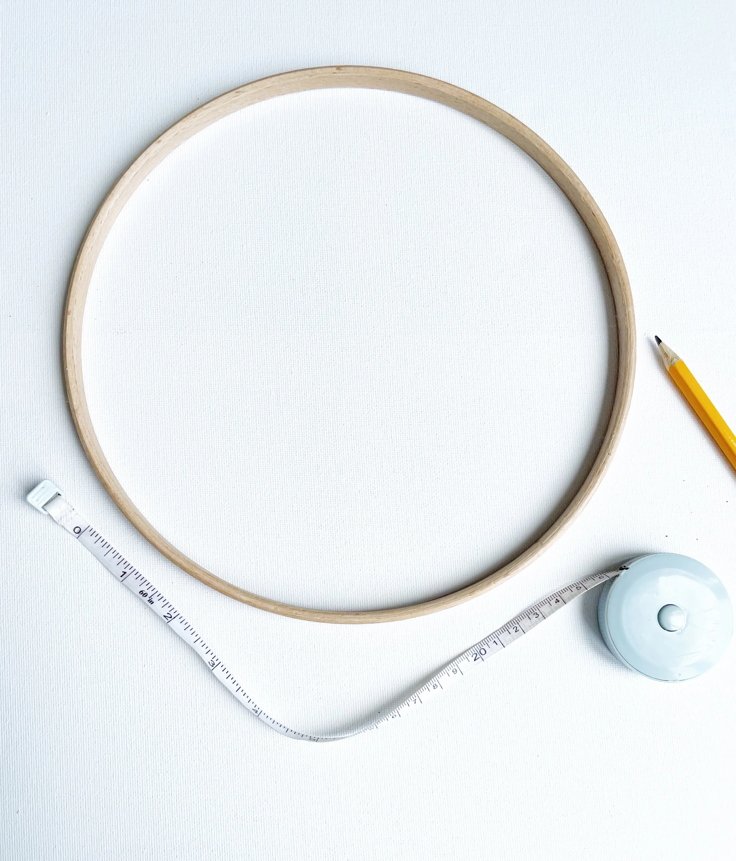 Wooden hoop, pencil and tape measure against a white background.