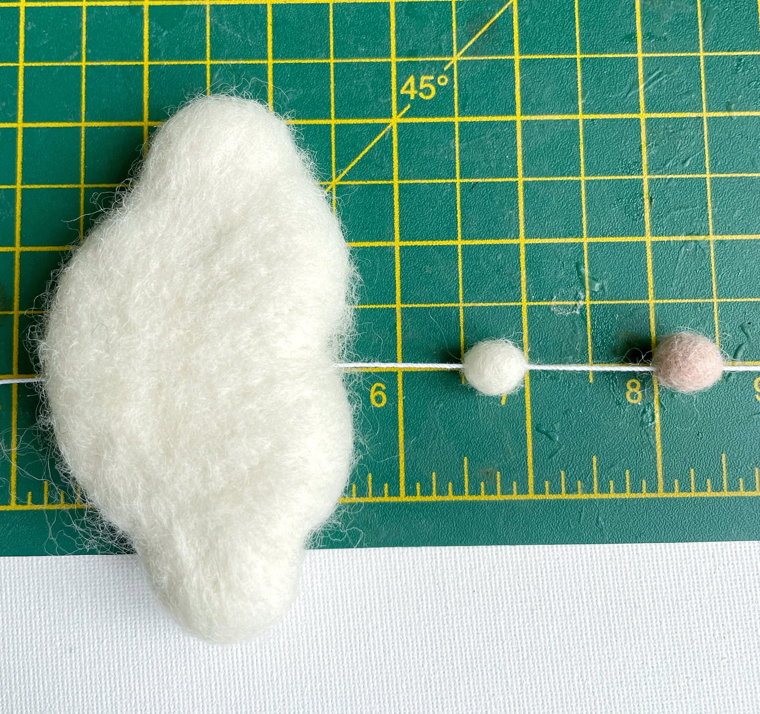 White wool felt cloud, pink and white felt balls threaded into white string. Measured on a green cutting mat.