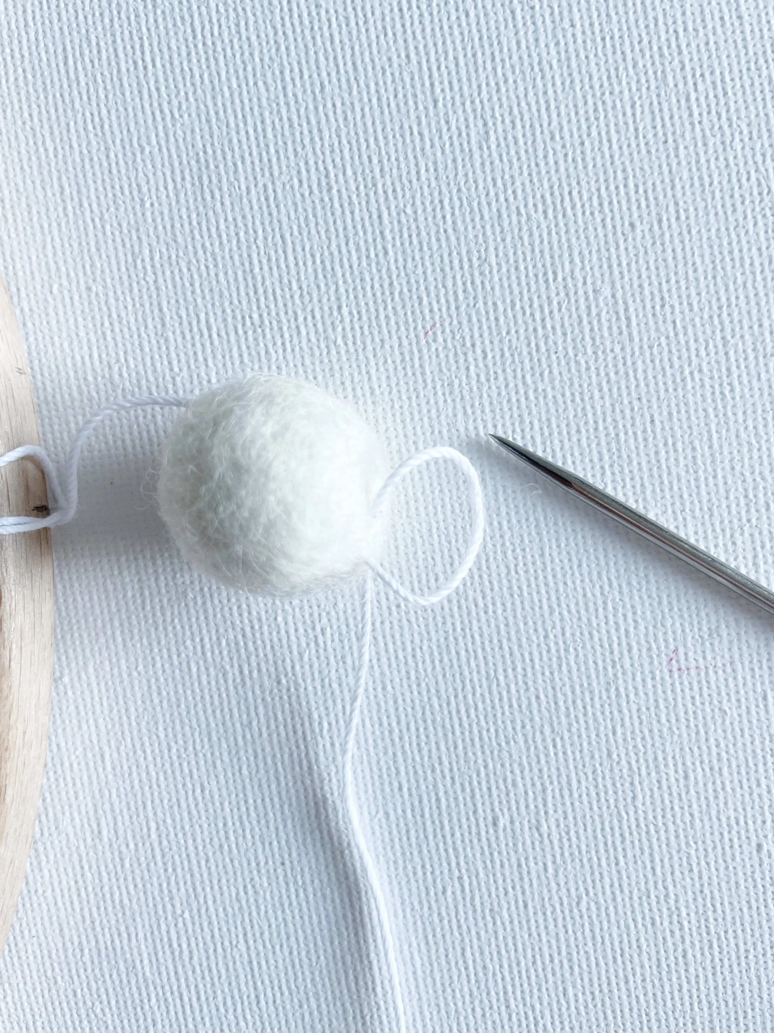 White felt ball with loop of white cotton at the base. Sewing needle sown at edge of image.
