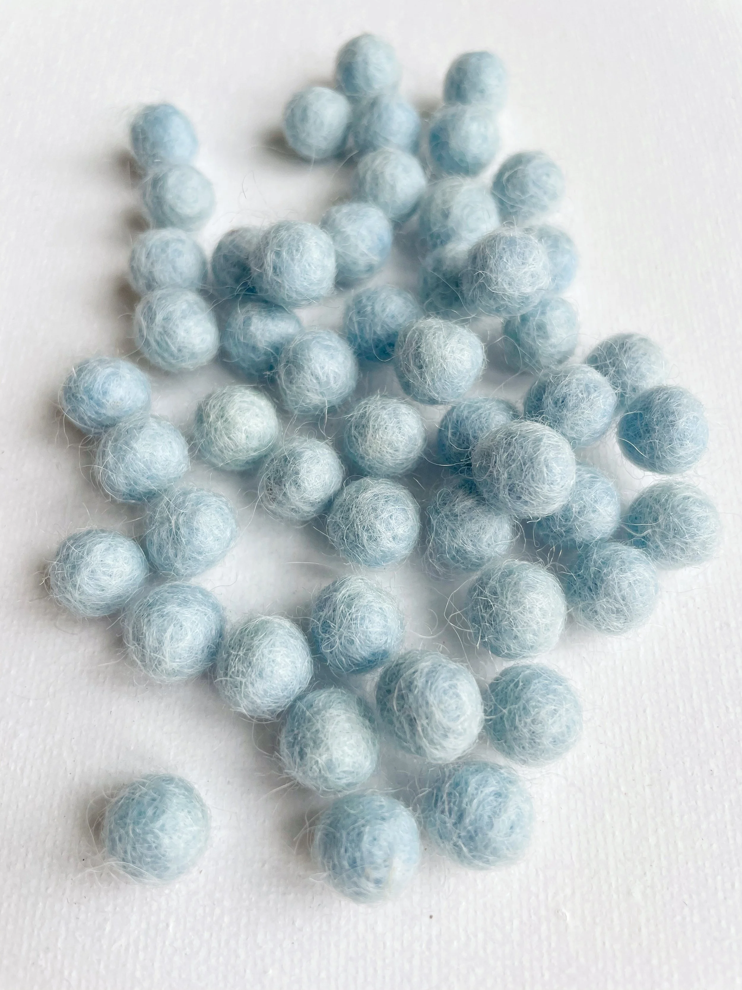 Light blue fuzzy felt balls scattered on a white surface.