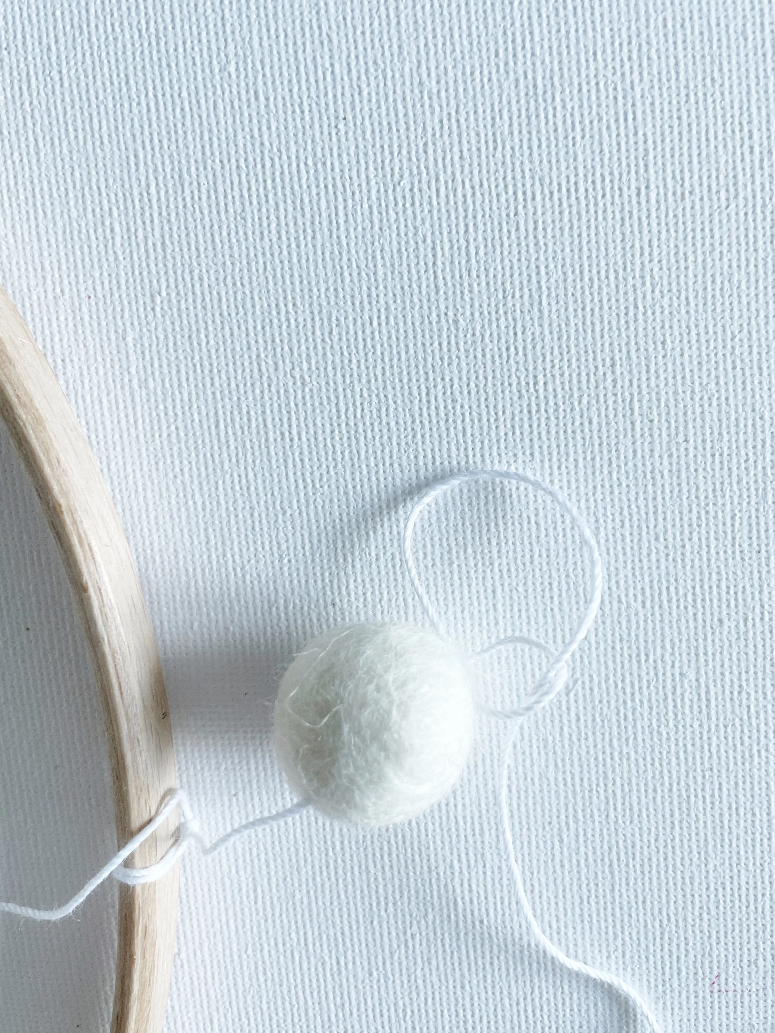 White felt ball with loop of white string at the base.