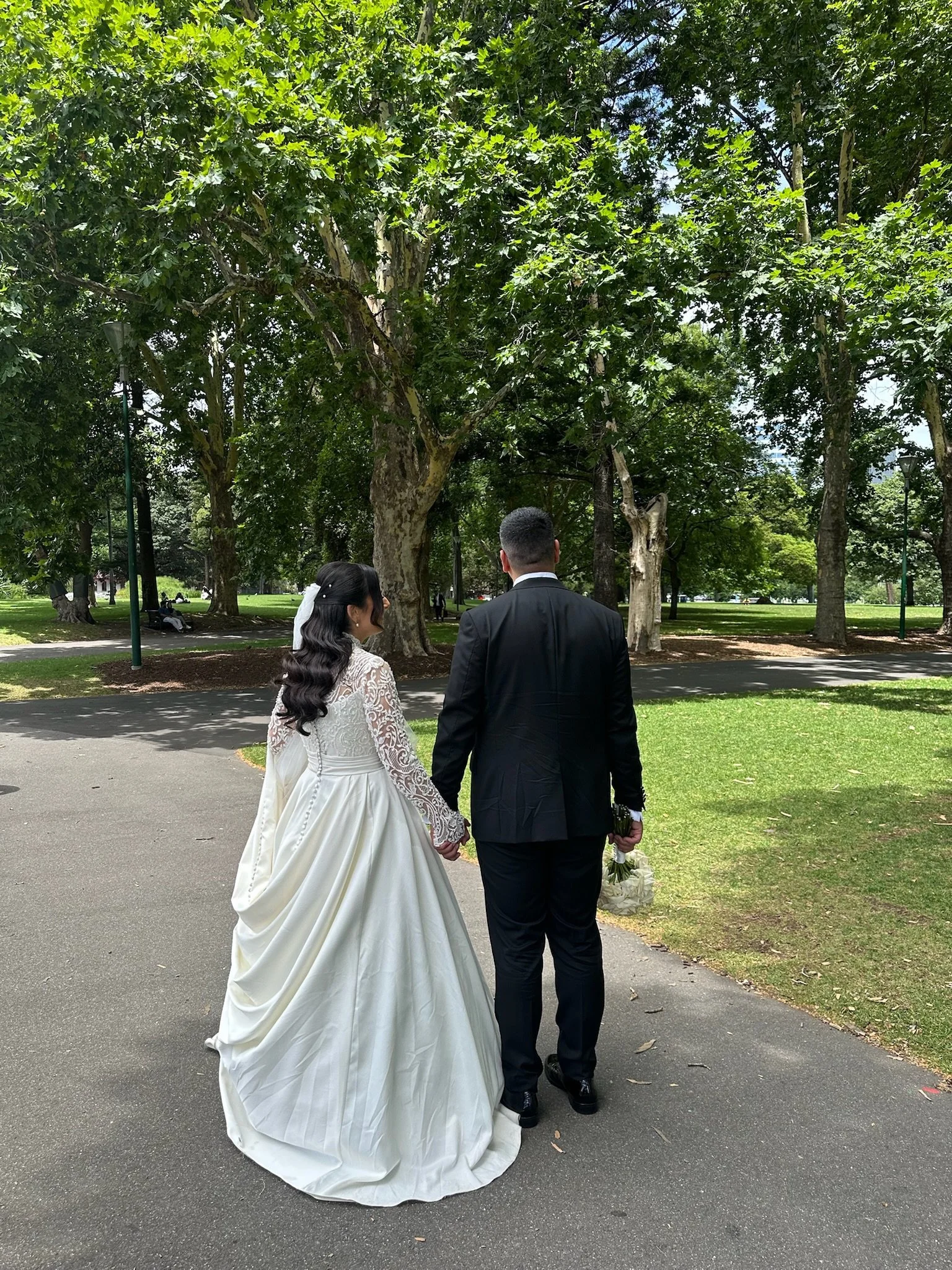 Bride and groom walking hand in hand in a park, wearing wedding attire. Captured by Melbourne Wedding Content Creator Dania.