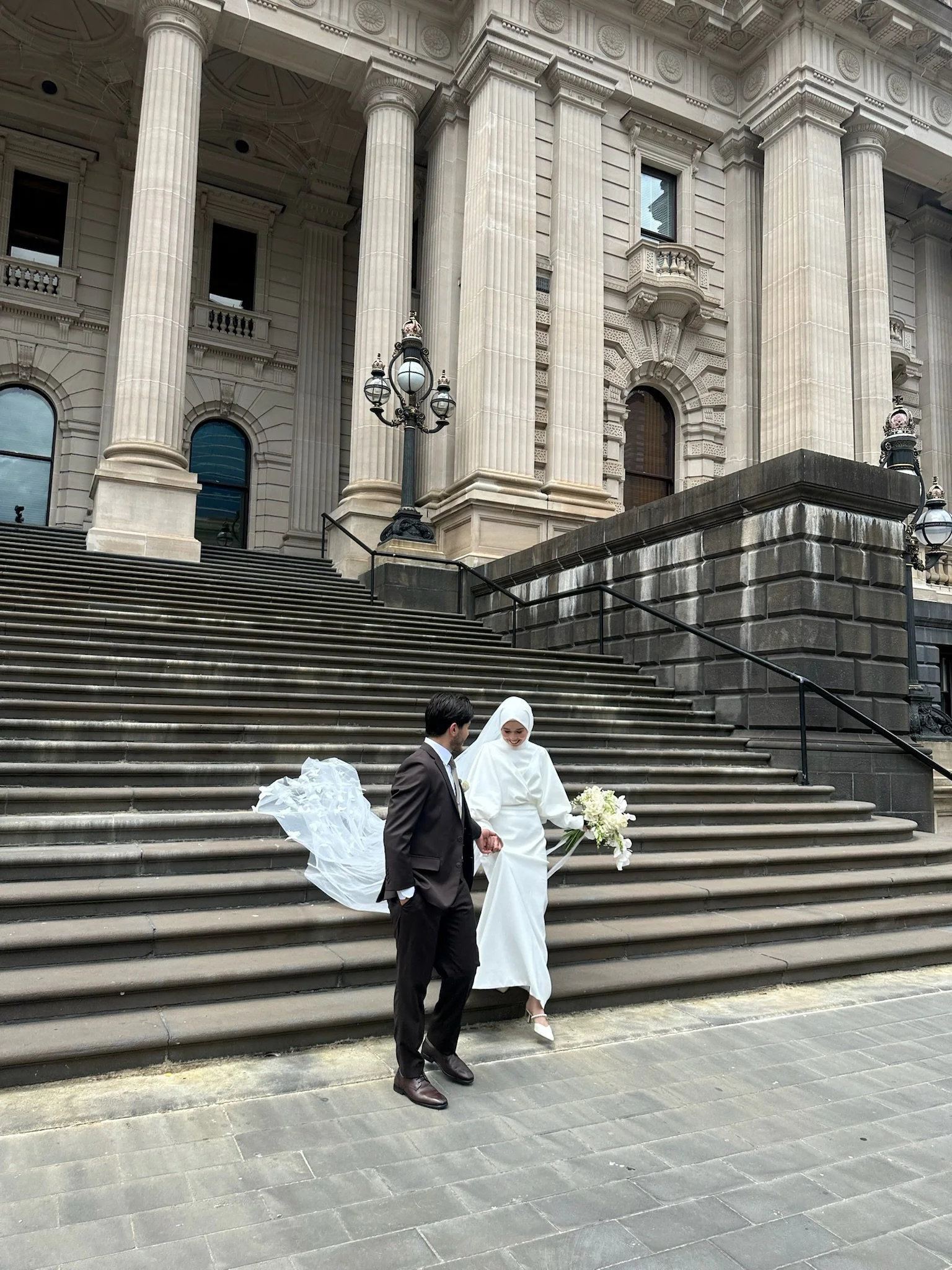 Bride and groom walking down grand stone steps outside a classical building. Captured by Melbourne Wedding Content Creator Dania.