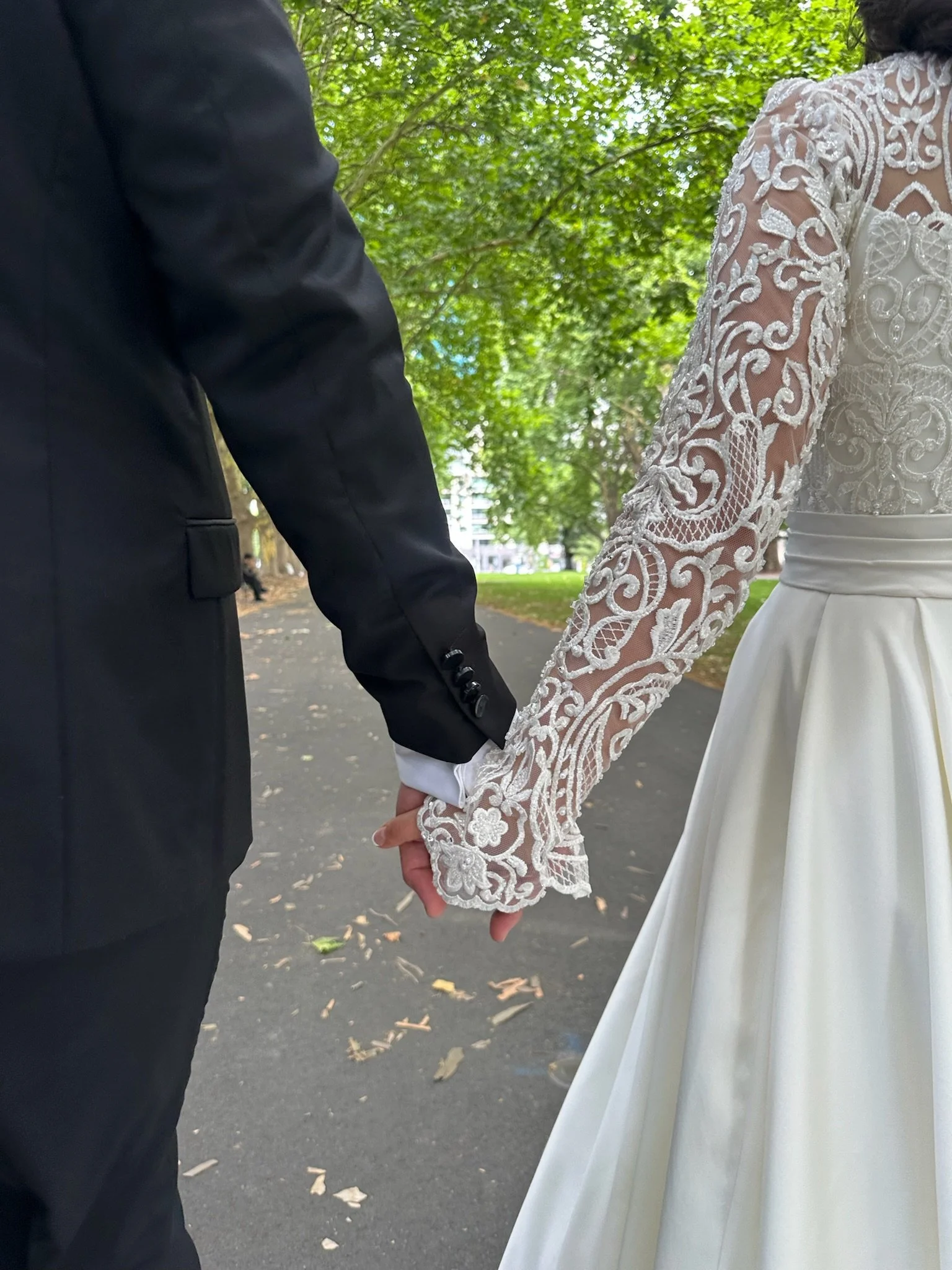 Bride and groom holding hands in a park, wearing wedding attire