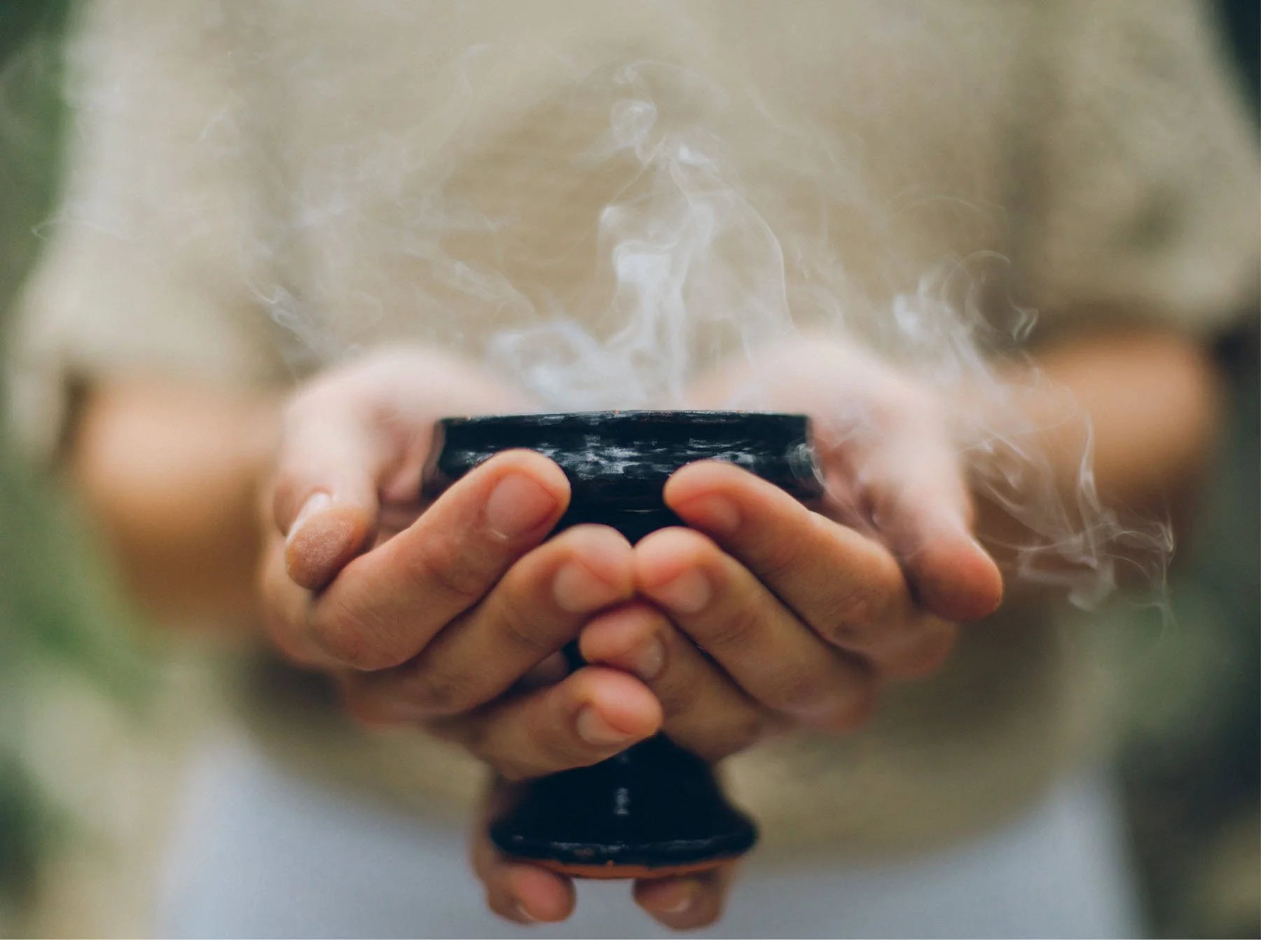 Person holding a black incense holder with smoke rising from it.