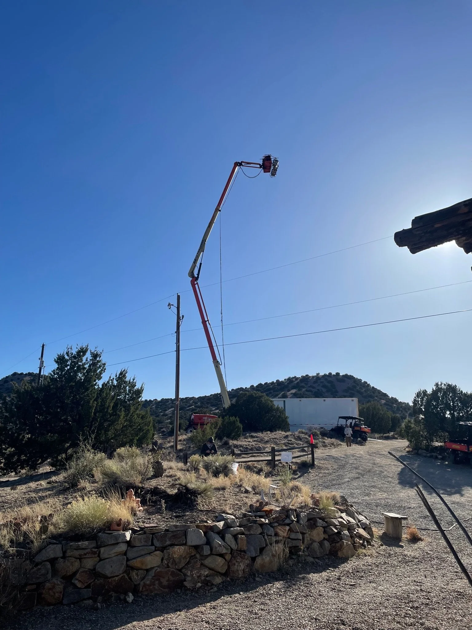Utility worker operating a bucket truck on a utility pole against a clear blue sky with a mountainous background.
