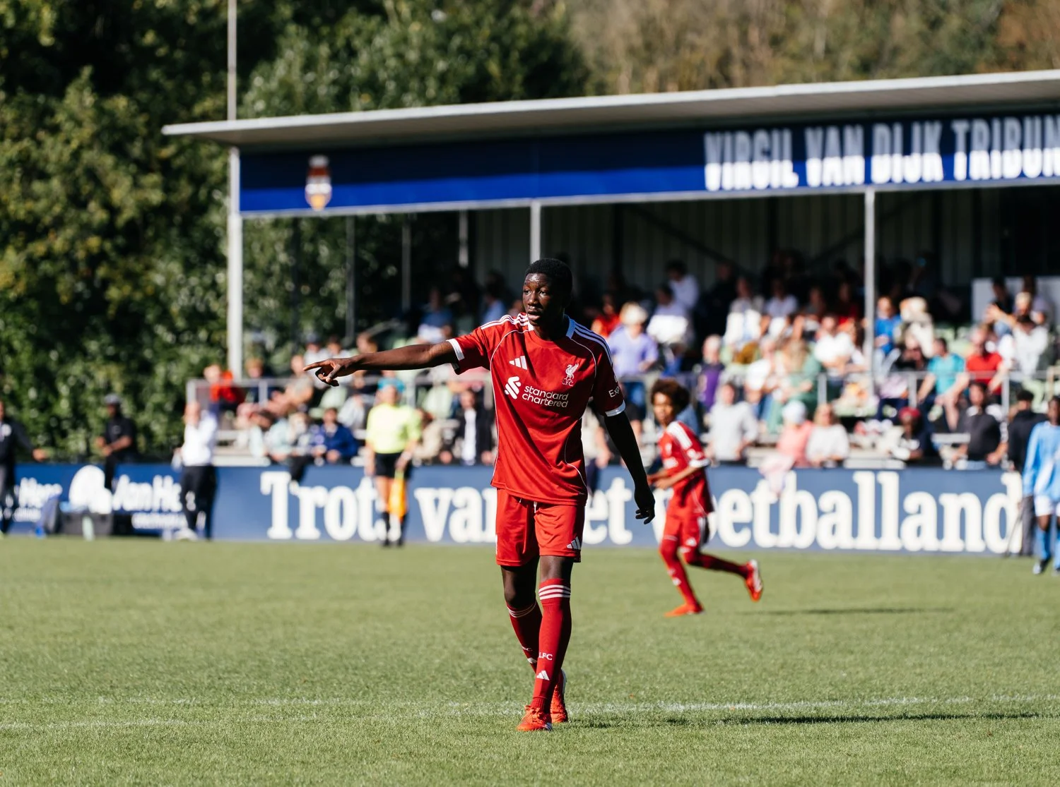 A soccer player in a red uniform on the field during a match, with spectators in the stands in the background.
