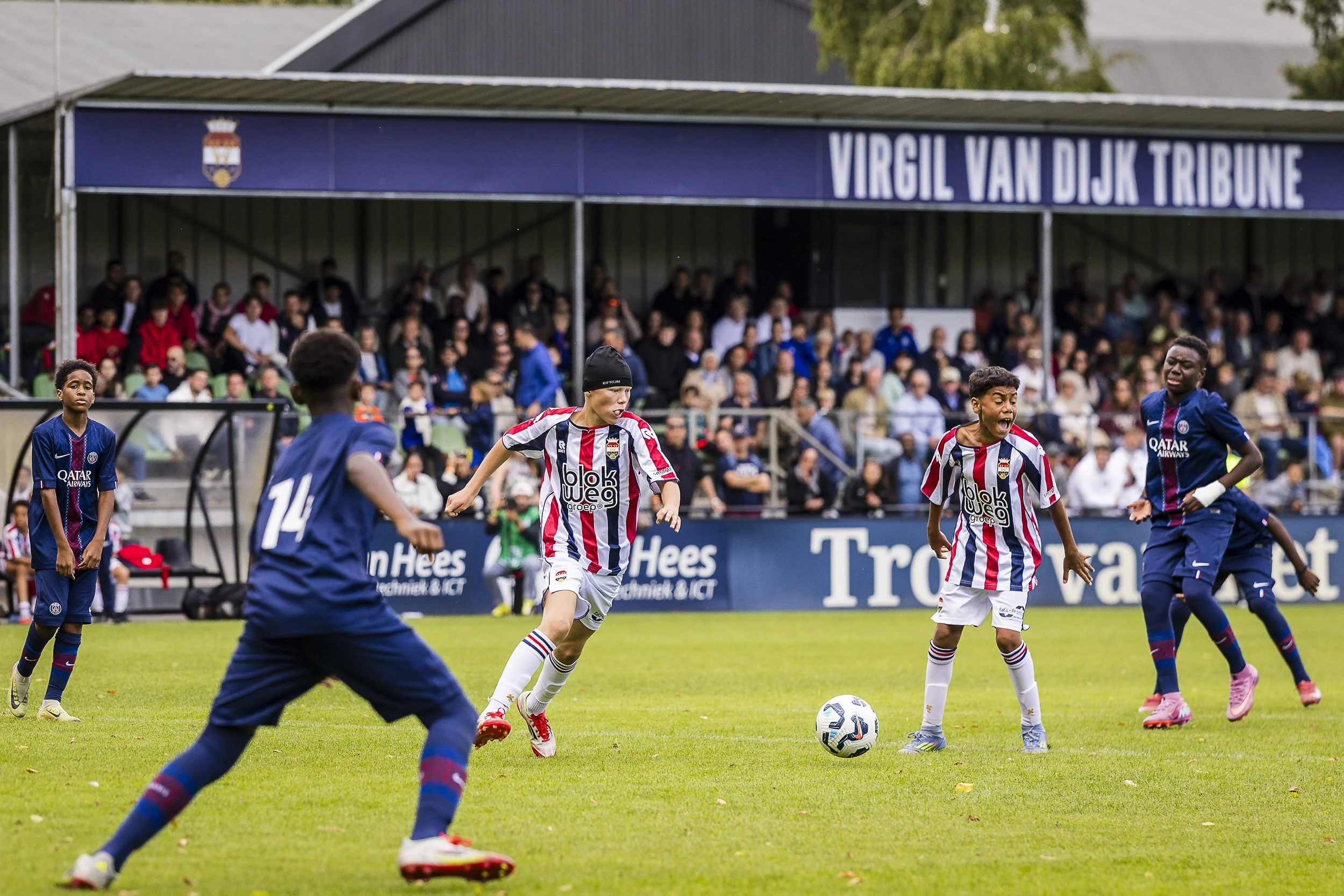 Young soccer players on the field with spectators in the background at a match in the Virgil Van Dijk Tribune in Tilburg.