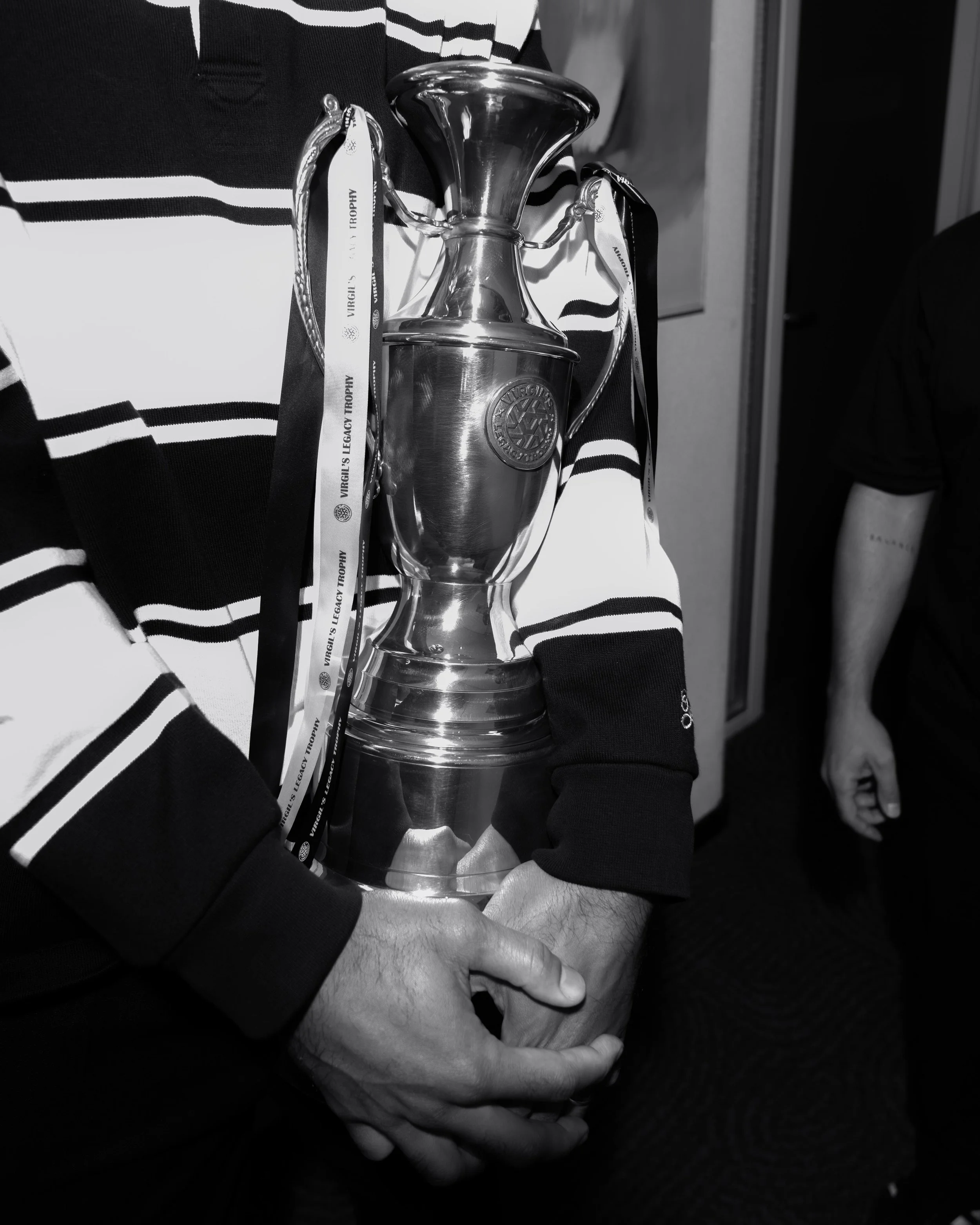 Person holding a silver trophy with ribbons that have text on them. Virgil van Dijk. During the Virgil's Legacy Trophy tournament in Tilburg.