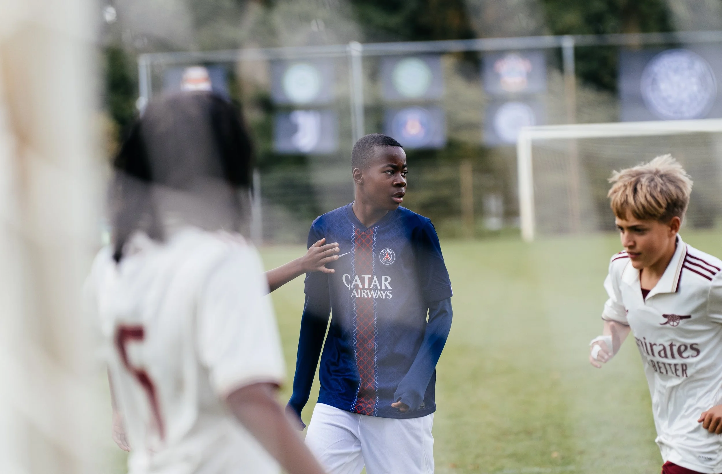 Young football players on the field, one wearing a Paris Saint-Germain jersey and other one from Arsenal, stand engaged in a game.