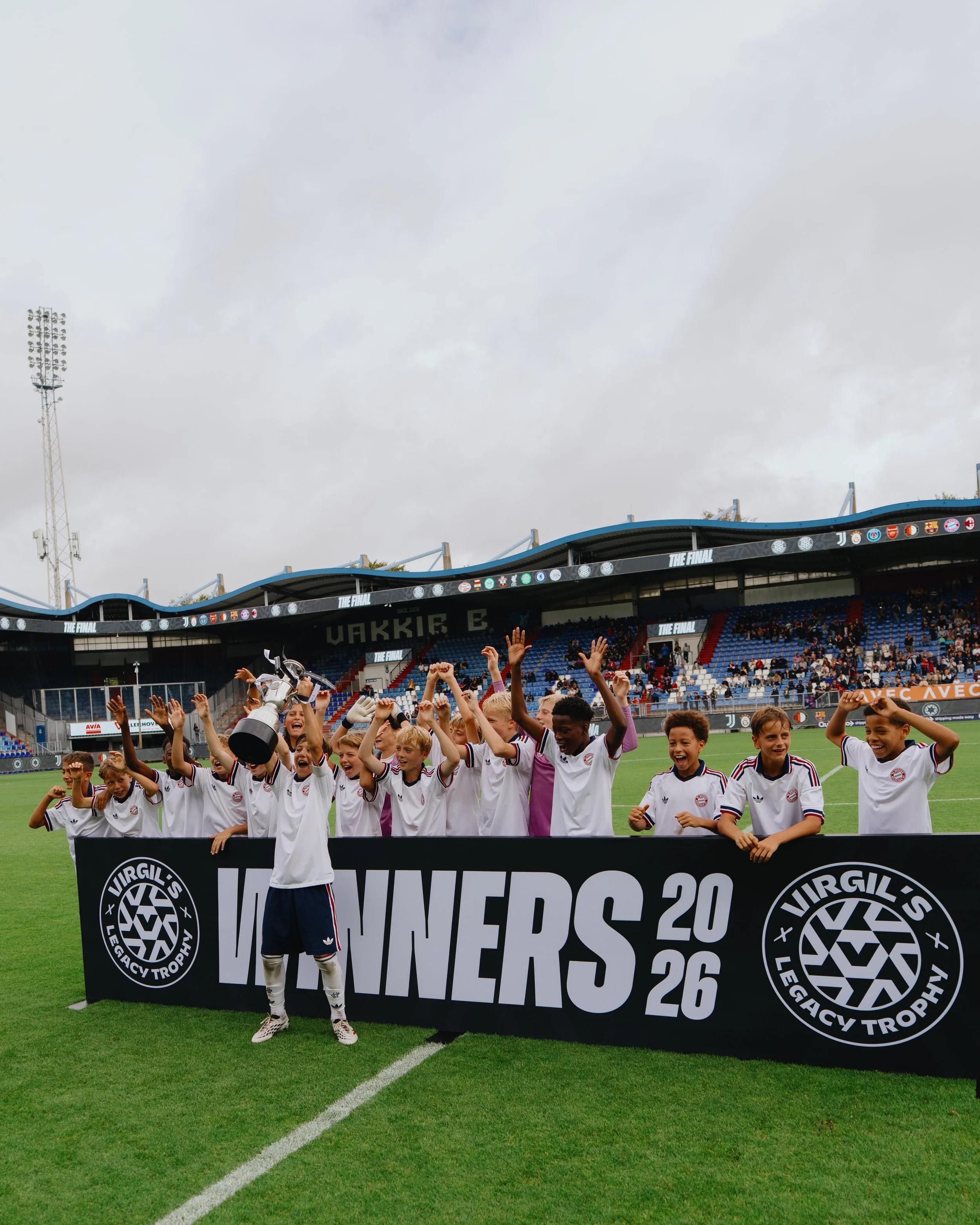 FC Bayern München wins Virgil's Legacy Trophy 2026, kids lifting the trophy inside the Koning Willem II Stadium.